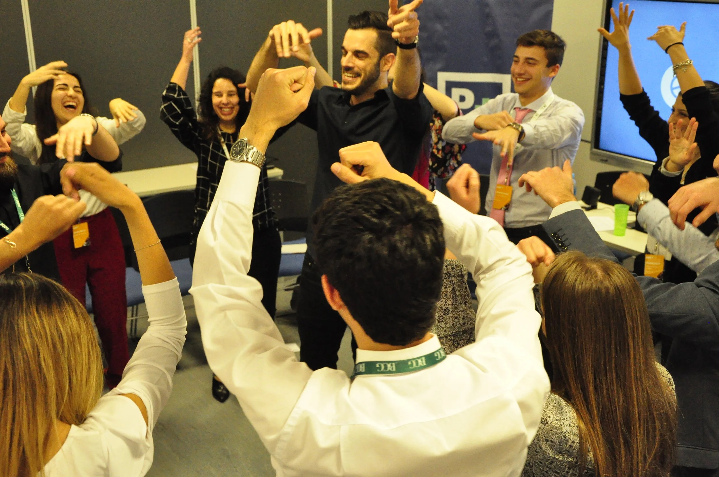 Grupo de personas participando en un evento, celebrando con gestos de alegría y entusiasmo en una sala de conferencia.