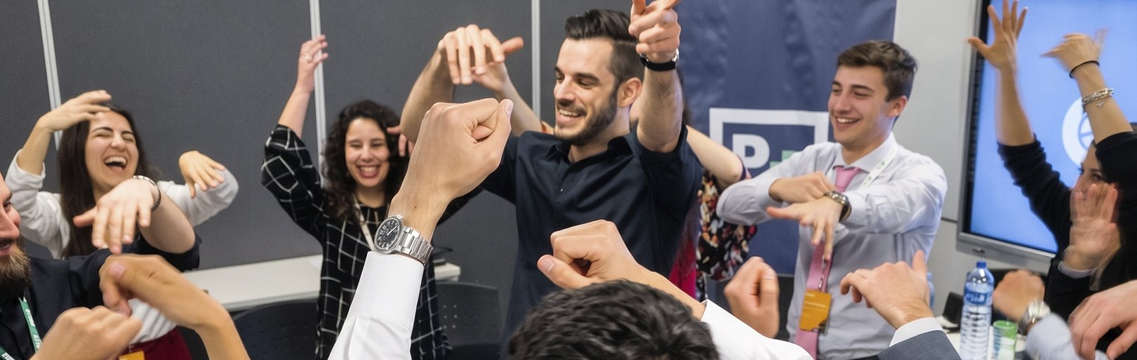 Grupo de personas celebrando con risas y gestos de alegría en una oficina, algunos levantando los brazos y otros con puños en señal de victoria.