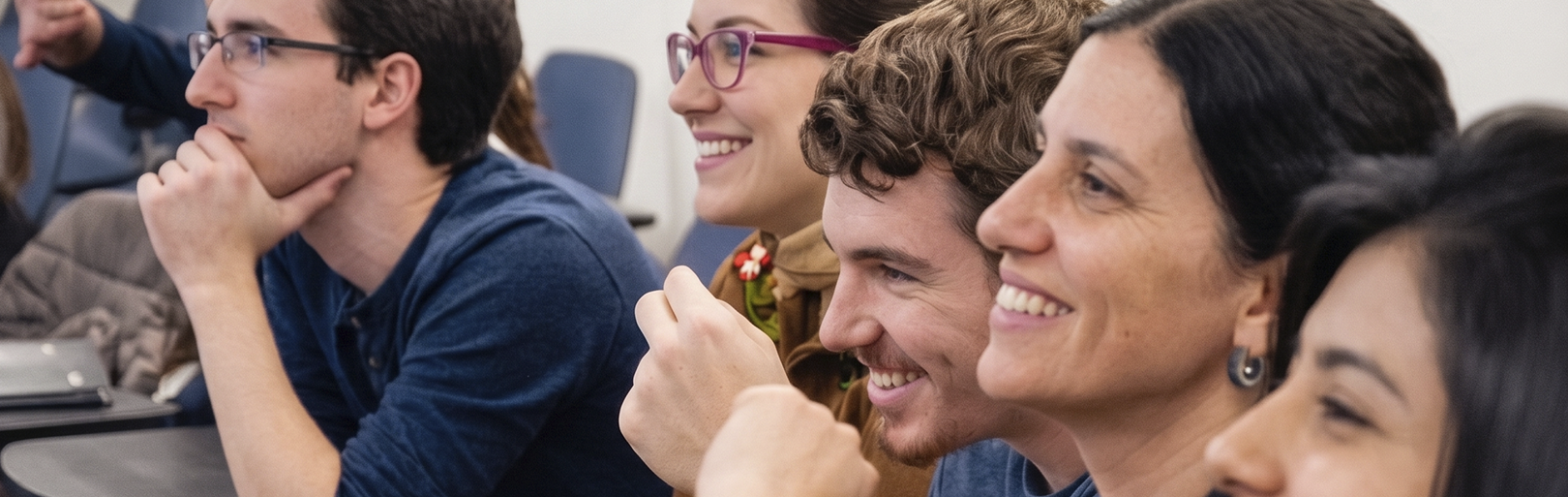 Grupo de personas en una conferencia o aula, sonriendo y atentos, algunos tomando notas