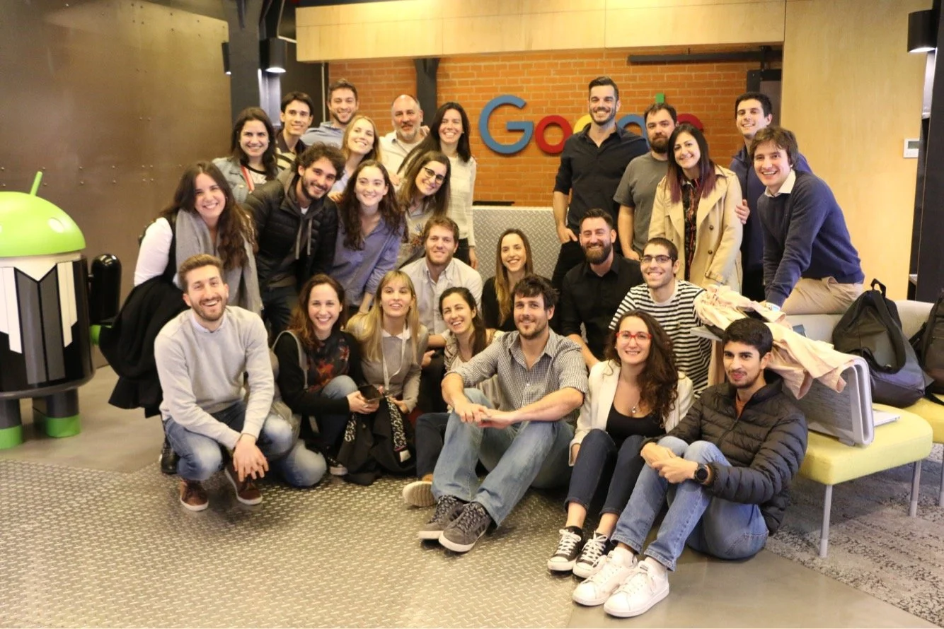 Grupo de personas posando juntas en una oficina con logotipo de Google en la pared