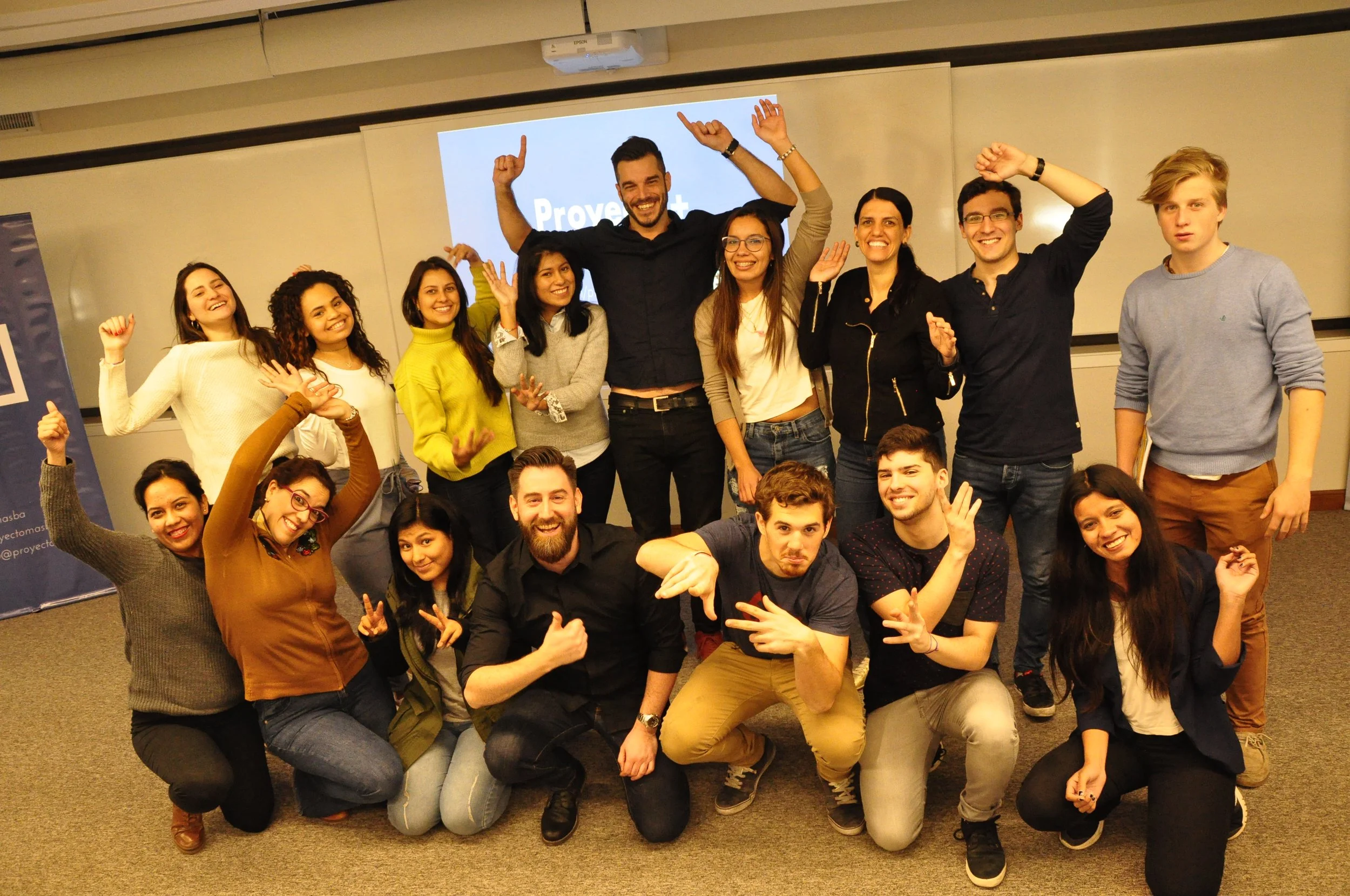 Grupo de personas en una sala, celebrando y sonriendo en una especie de evento o taller, con un proyector detrás.