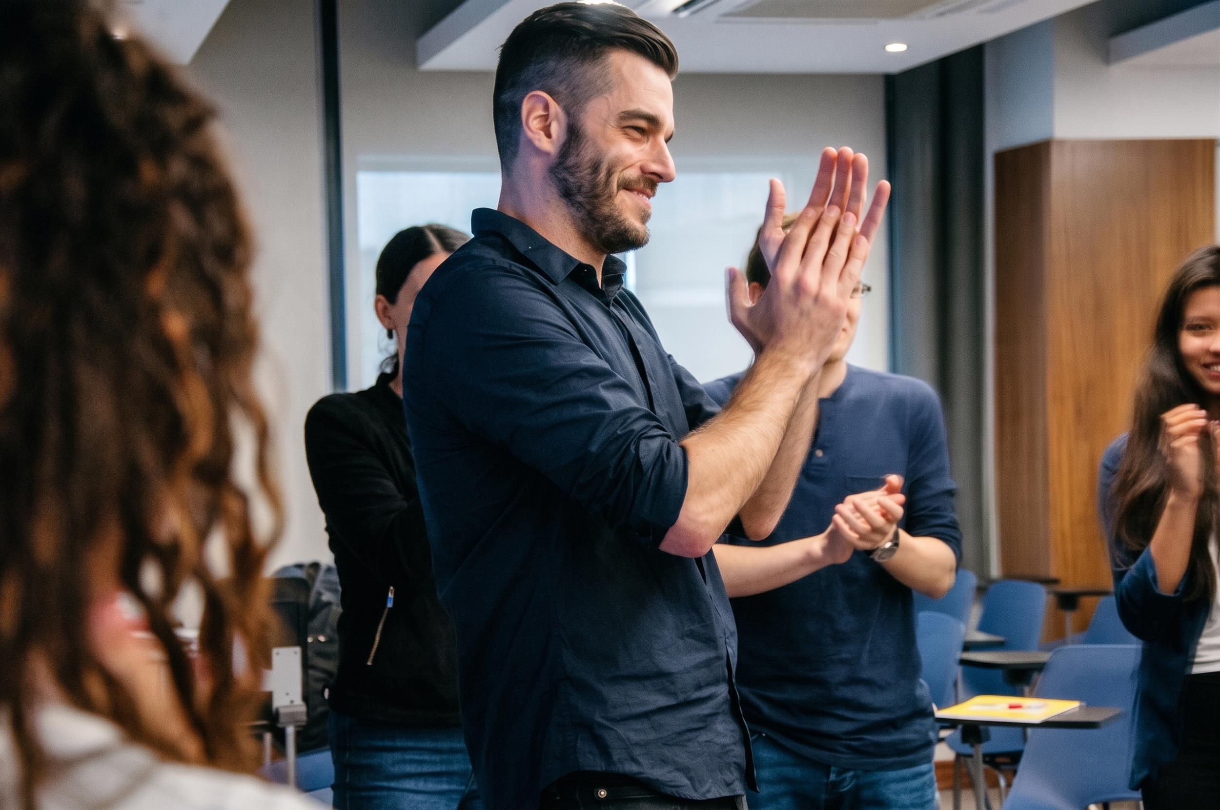 Hombre sonriendo y aplaudiendo en una reunión con varias personas en un ambiente de oficina moderna.