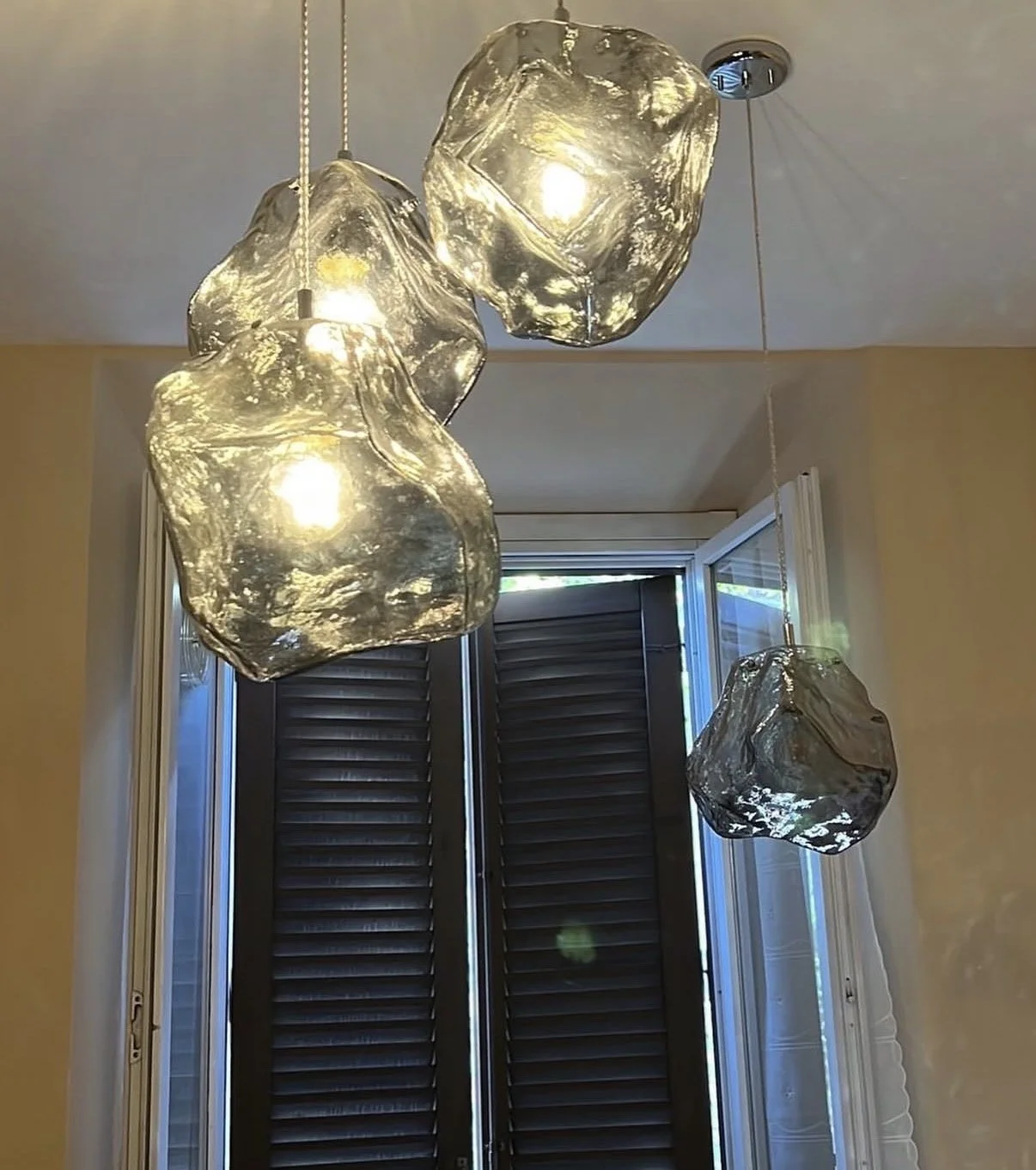 Three modern pendant lights with irregular glass shades hanging from the ceiling in front of a window.