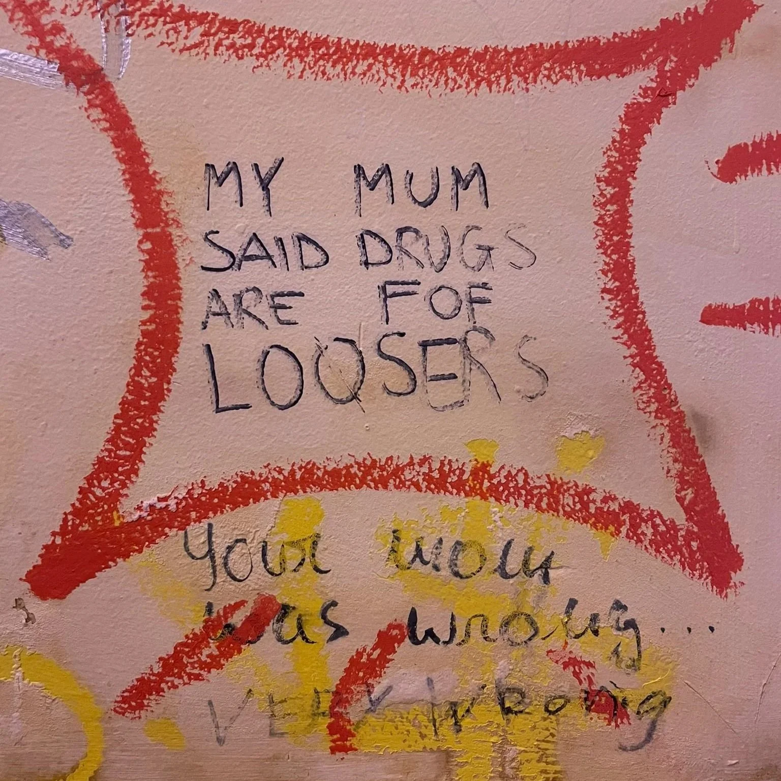 A wall with red, orange, and yellow graffiti and a handwritten message that reads, "My mum said drugs are for losers. You know as wrong..."