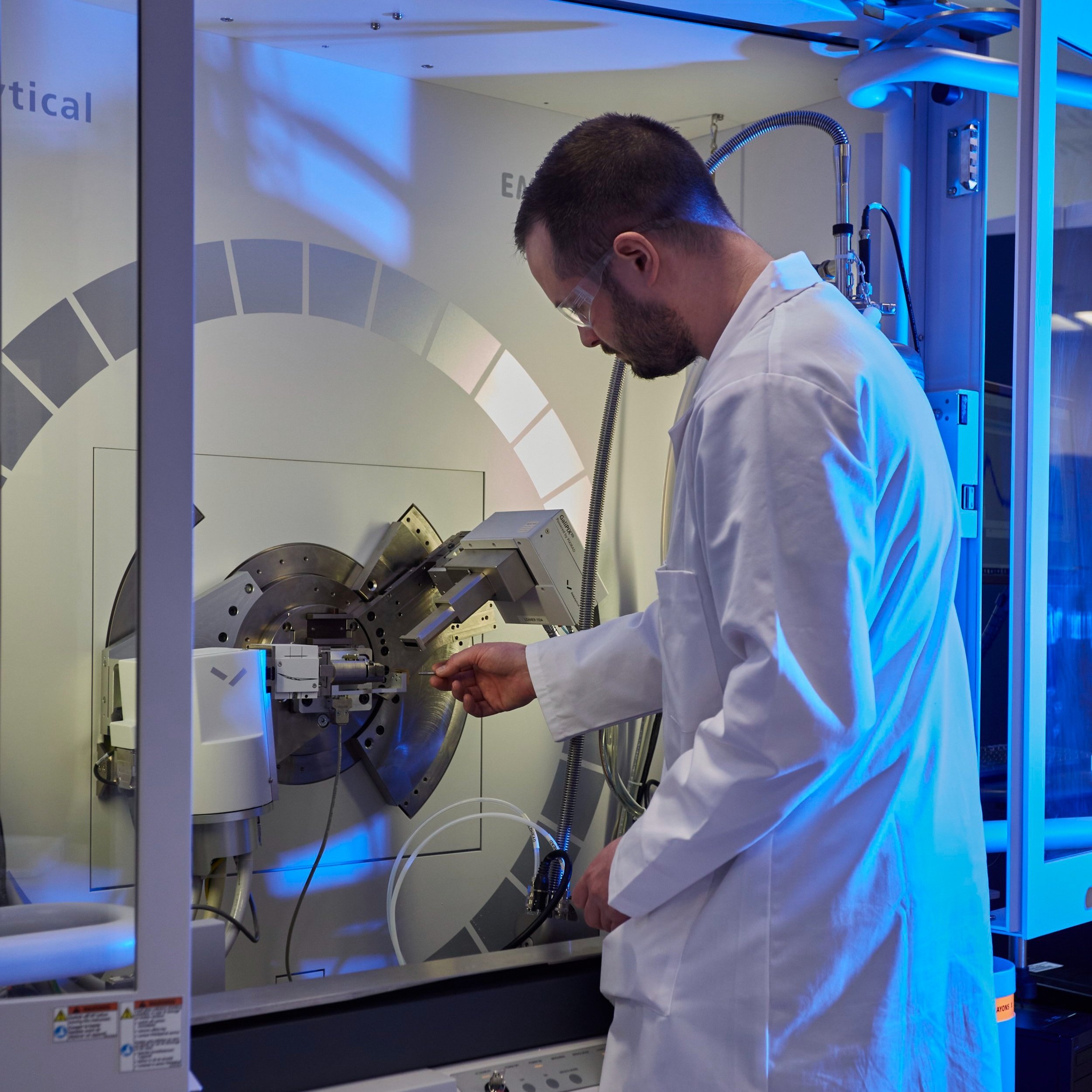 A scientist wearing protective glasses and a head covering working in a laboratory with scientific equipment and test tubes.