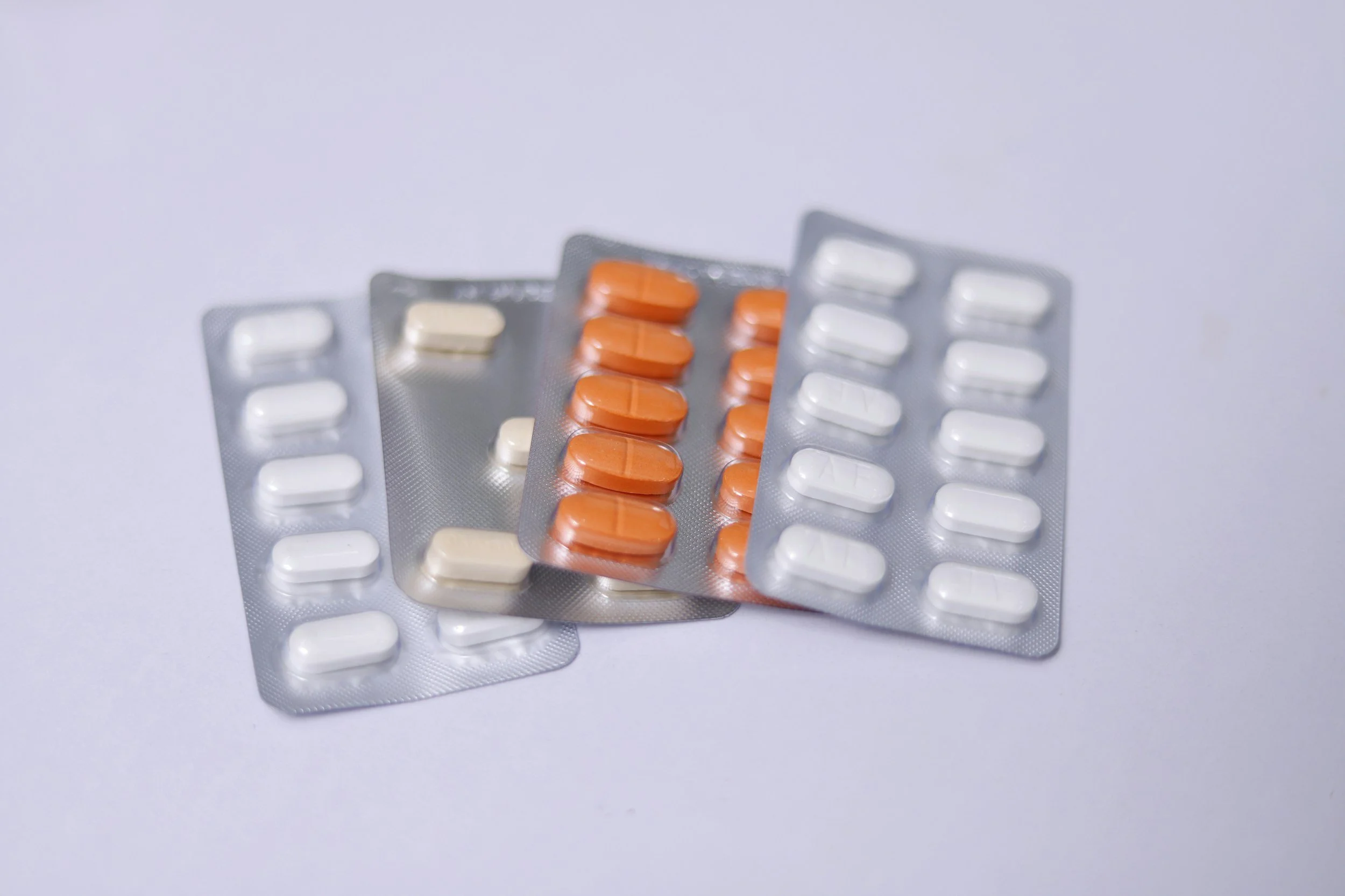 Multiple blister packs of pills, including white and orange tablets, stacked on a white surface.