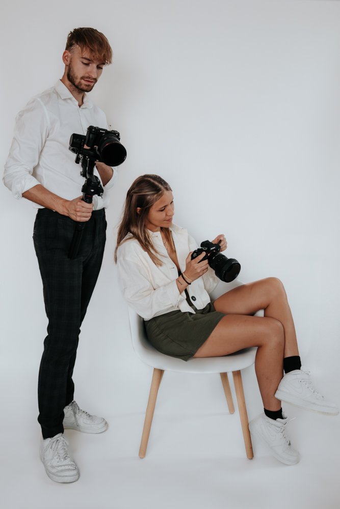 Un couple de photographes posant dans un studio lumineux, chacun tenant un appareil photo – duo créatif derrière LG photo & film.
