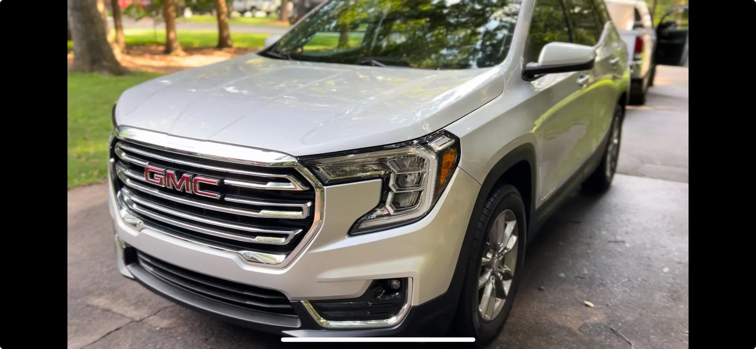 Silver GMC SUV parked on a driveway with trees and grass in the background.
