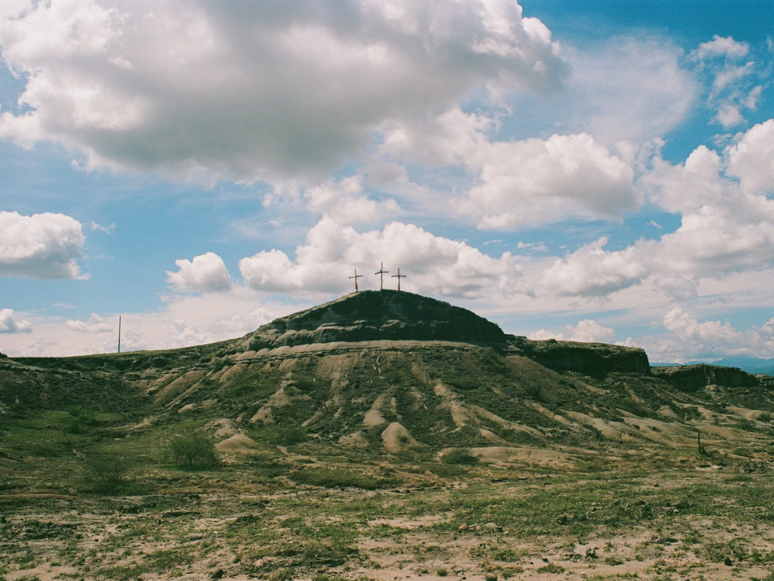 Three crosses on top of a grassy hill under a partly cloudy sky.