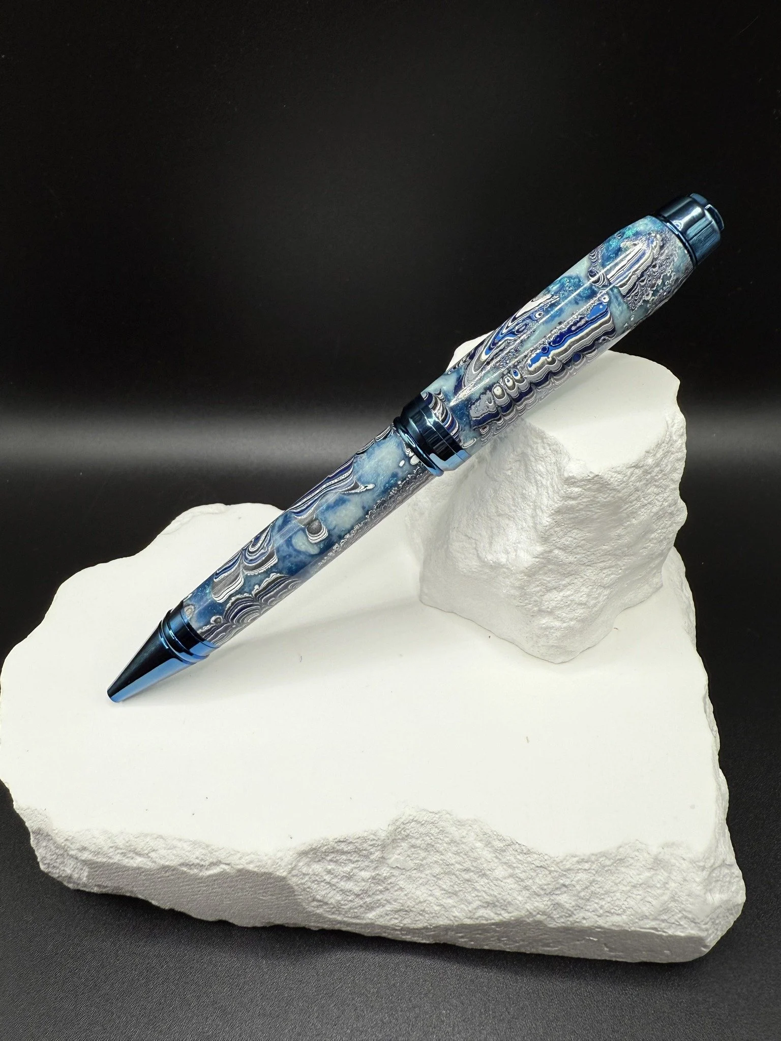Kenworth Dragonscale Fordite cigar pen, Blue and gray patterned, resting on a white textured surface with a black background.
