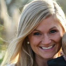 Close-up of a smiling woman with long blonde hair, outdoors in sunlight.