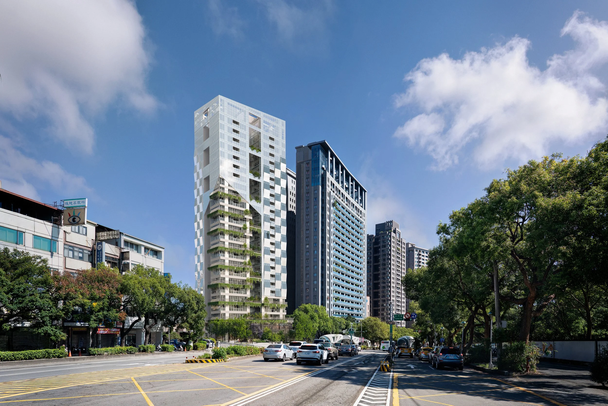 City street with modern high-rise buildings, cars on the road, trees lining the sidewalk, and a partly cloudy blue sky.