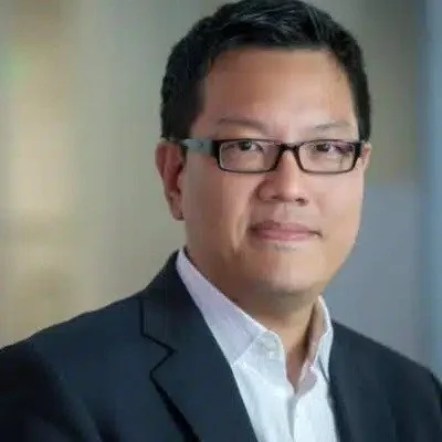 Portrait of a man wearing glasses, a dark suit, and a white shirt.