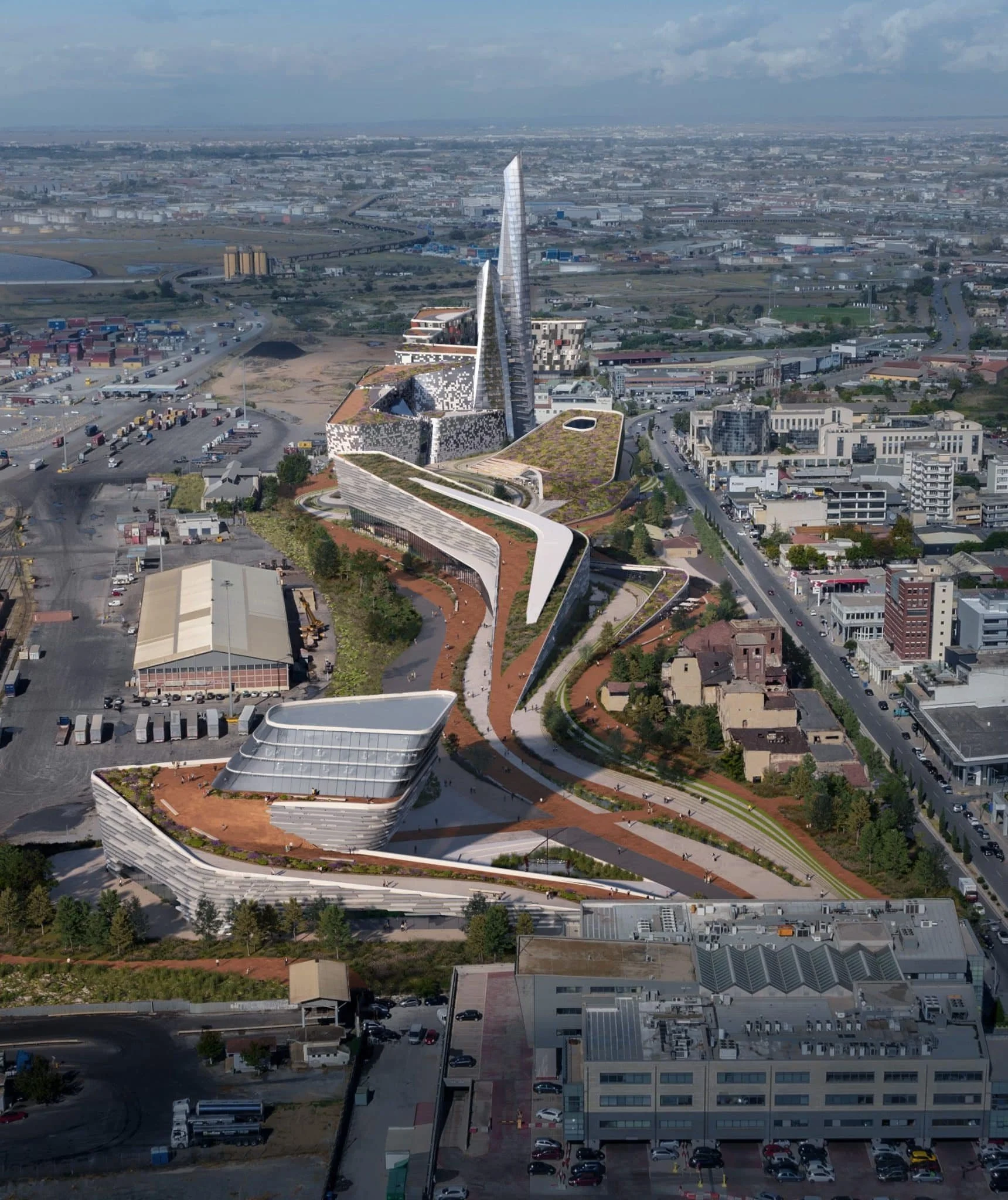 Aerial view of a modern cityscape with a distinctive architectural building with tall spires and various curved structures, surrounded by roads, smaller buildings, and green areas.