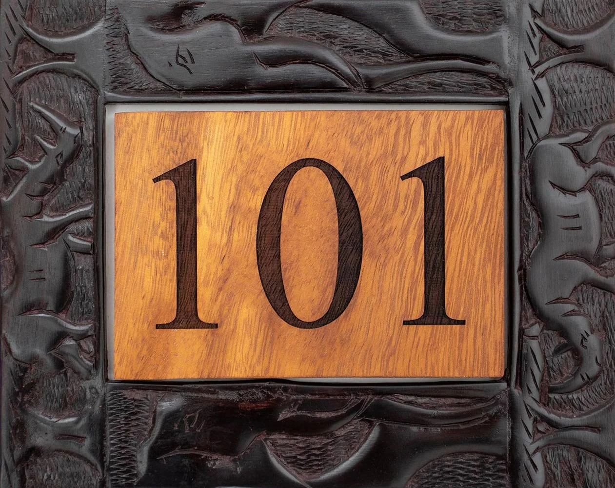 A house number plaque displaying the number 101, with a wooden background and a decorative dark frame.