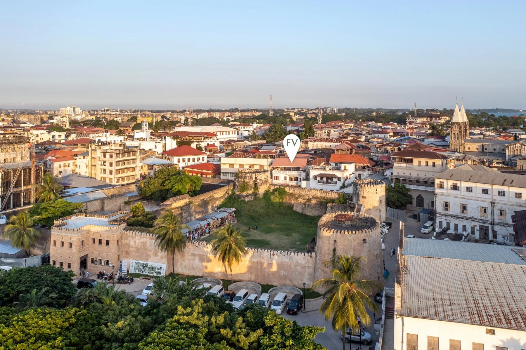 Cityscape with historic castle walls, palm trees, and a church in the background during daytime.