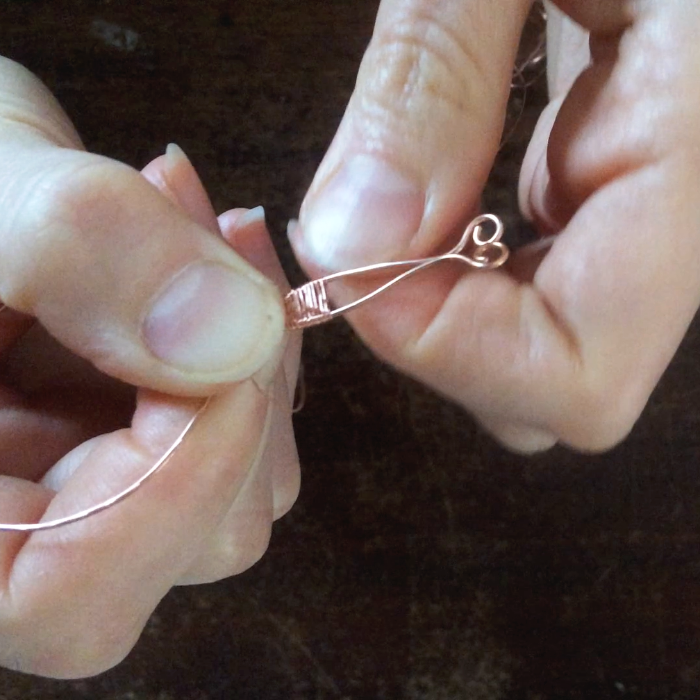 Person som arbetar med att skapa ett smycke av metalltråd, där trådarna vävs samman