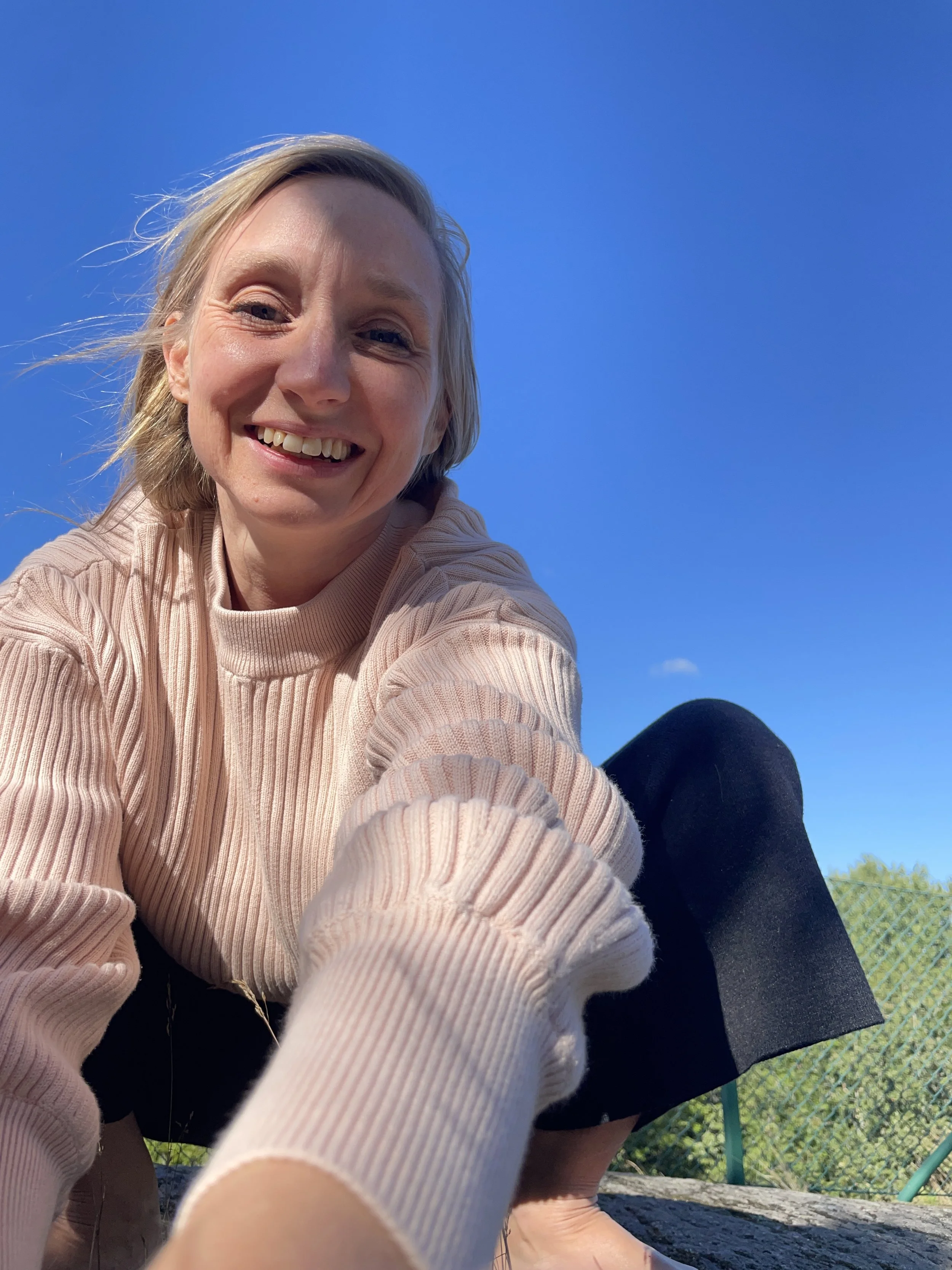 Josefine Nyberg ler mot kameran, utomhus under en klar blå himmel, klädd i en rosa ribbad tröja.