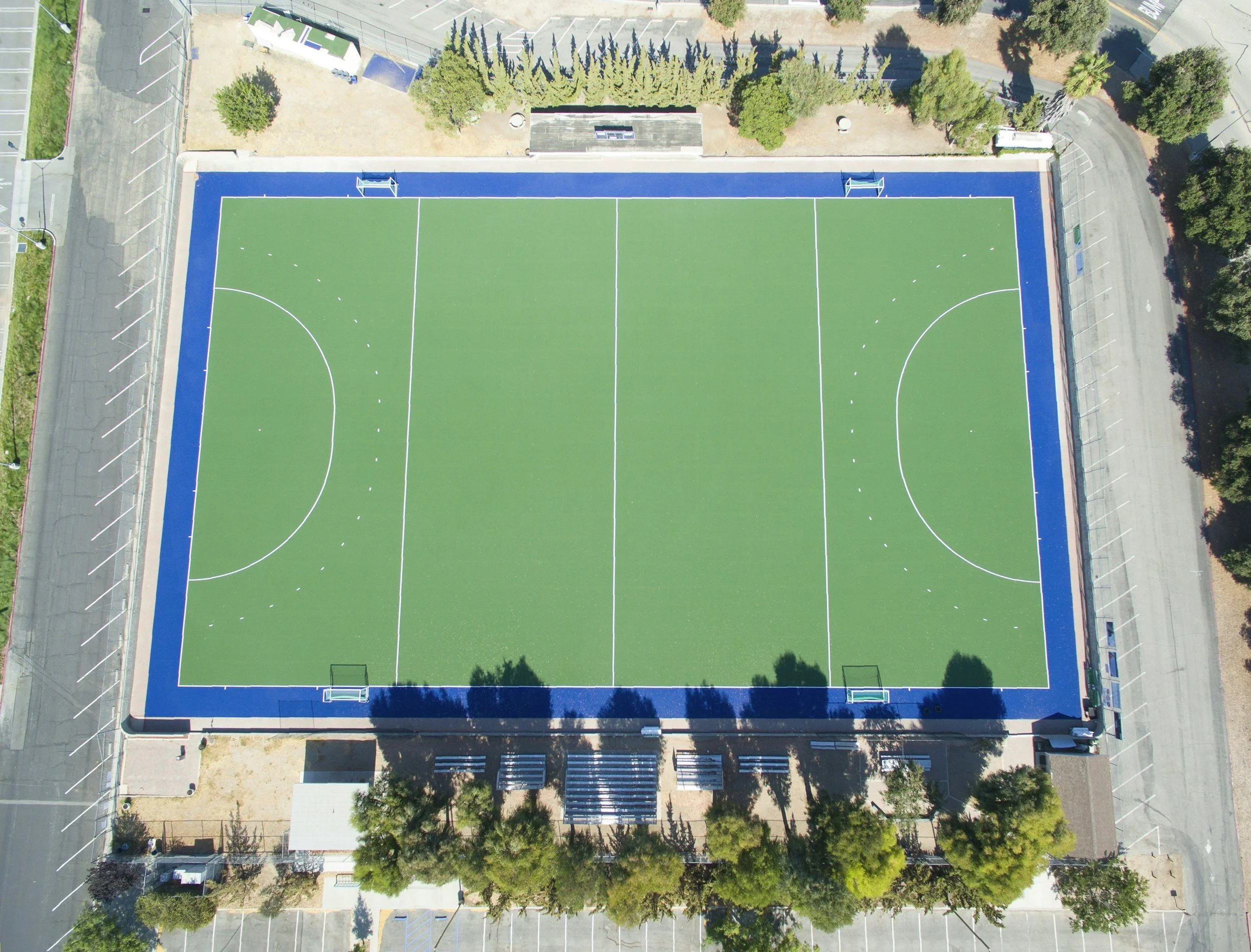 Cancha de fútbol sala vista desde arriba, rodeada de árboles, caminos y estacionamientos.