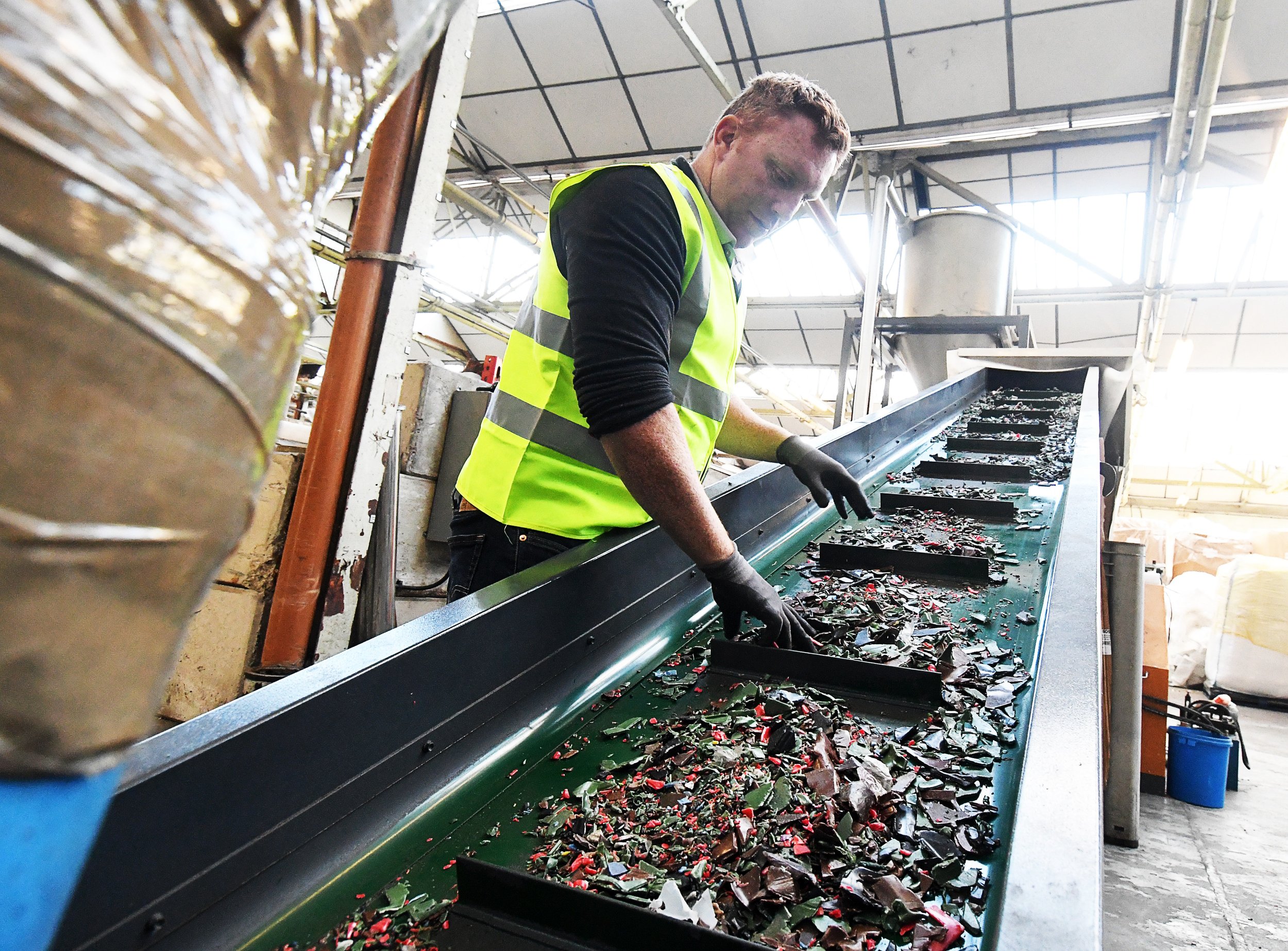 Man in high-visibility jacket checking the quality of material on a conveyor-belt as part of the wheelie bin recycling process