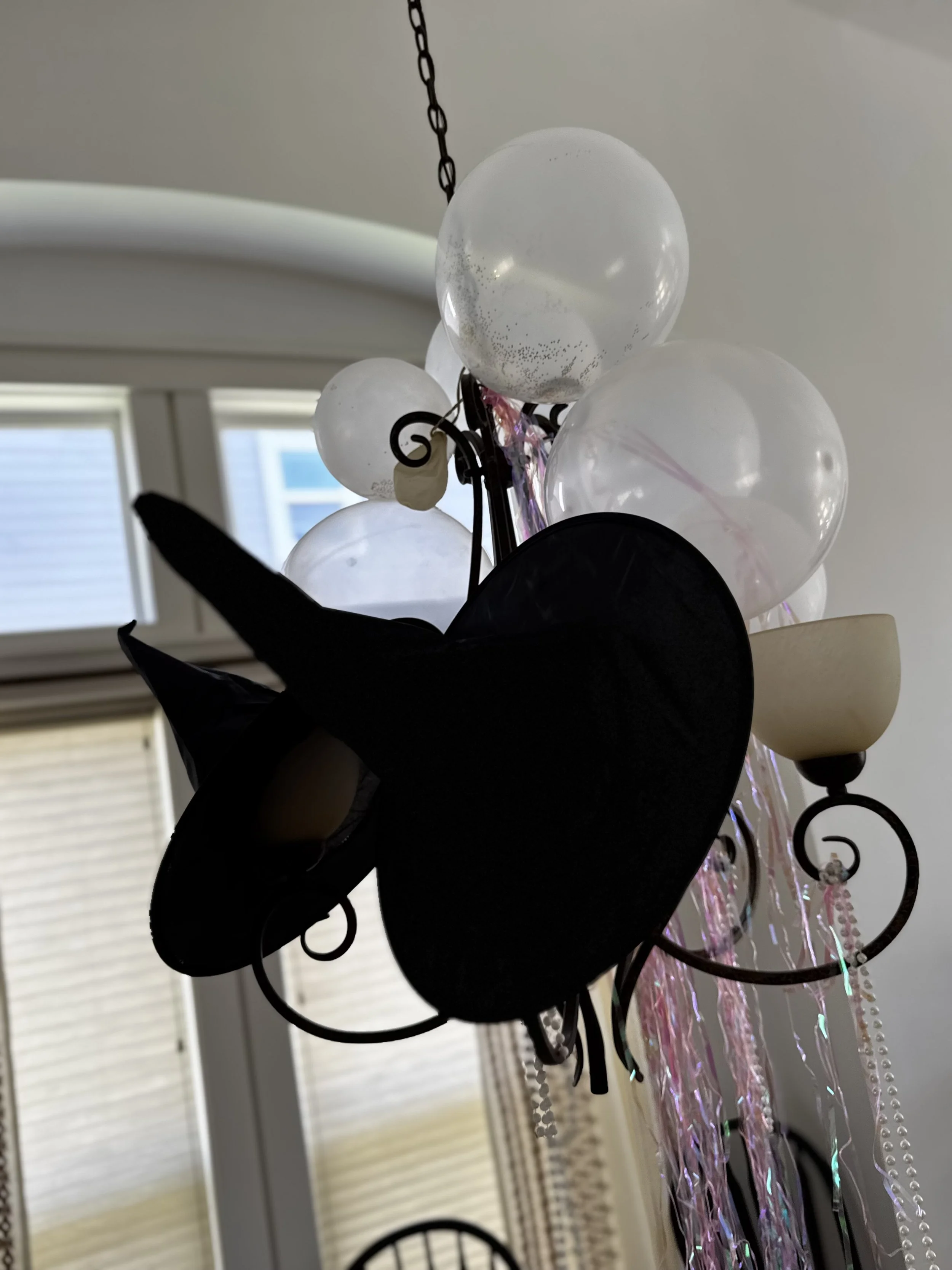 Close-up of a chandelier with white glass globes and hanging crystal beads in a room with windows in the background.
