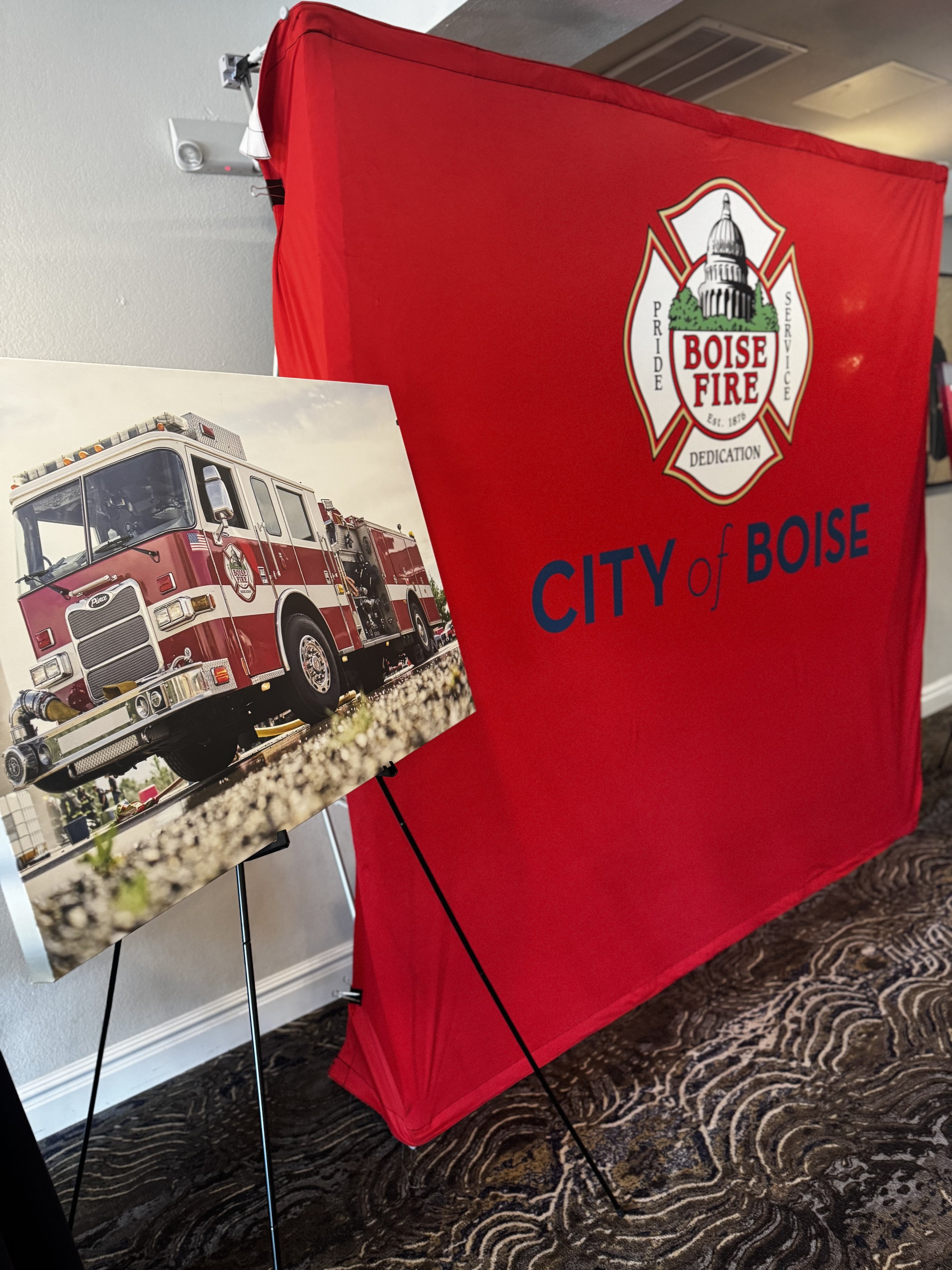 A backdrop displaying a Boise Fire Department crest, and a framed photo of a red fire truck on a stand. This is for a Boise Fire Department retirement party at The River Club in Boise Idaho