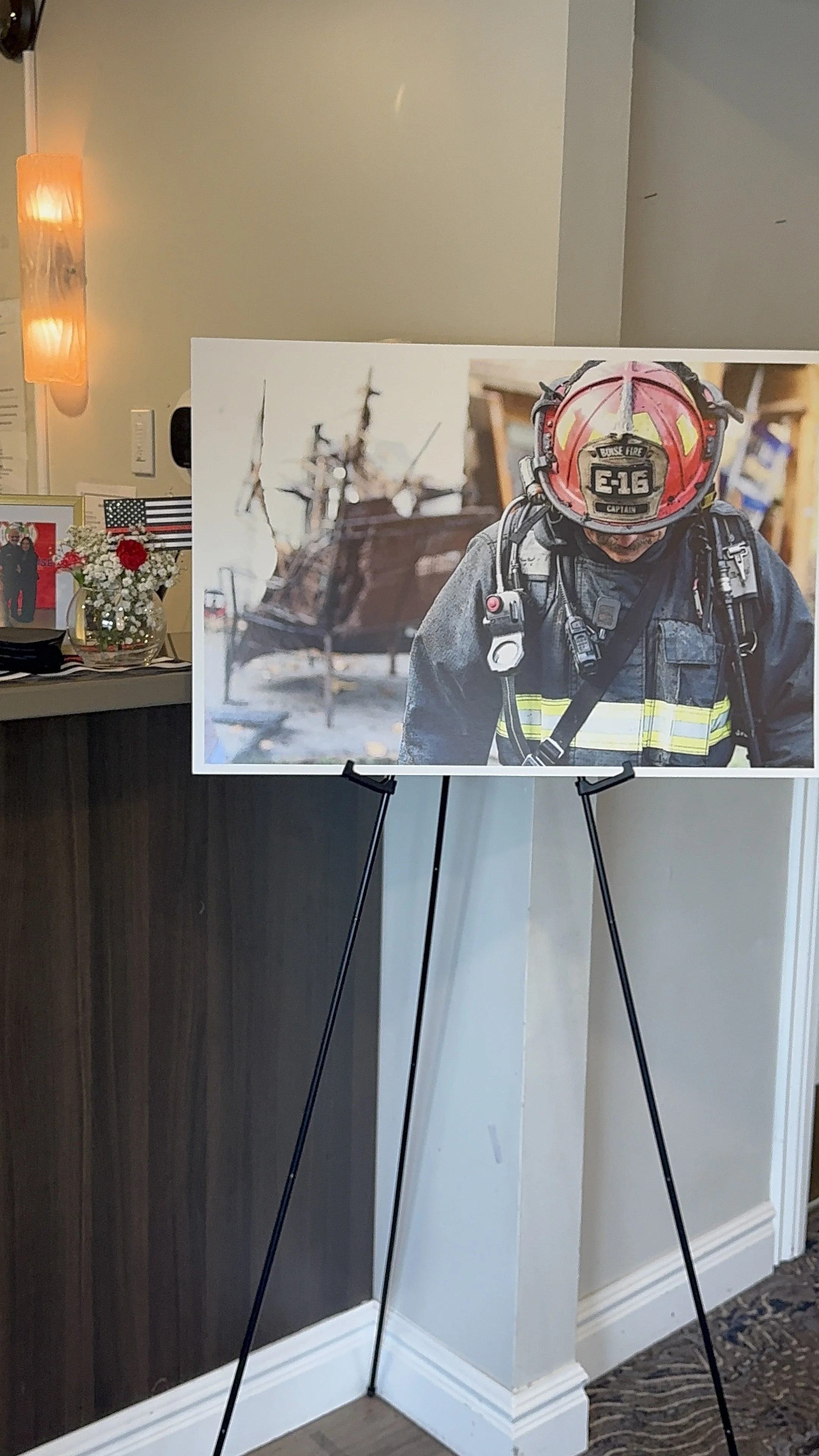 Photo of an easel displaying a firefighter with a helmet and gear, with a helicopter in the background.