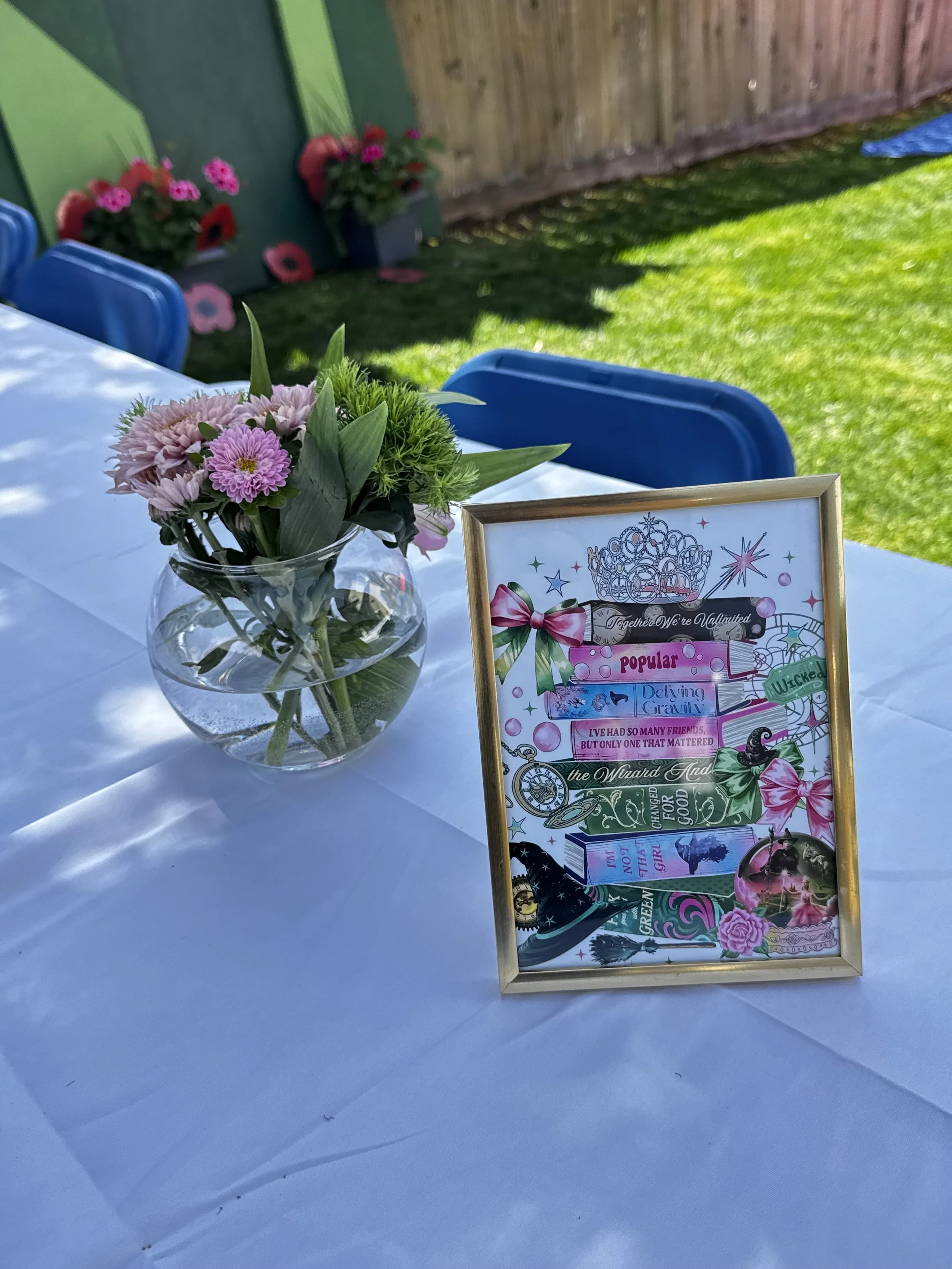 A table decorated with a pink flower arrangement in a glass vase and a colorful, carnival-themed sign.