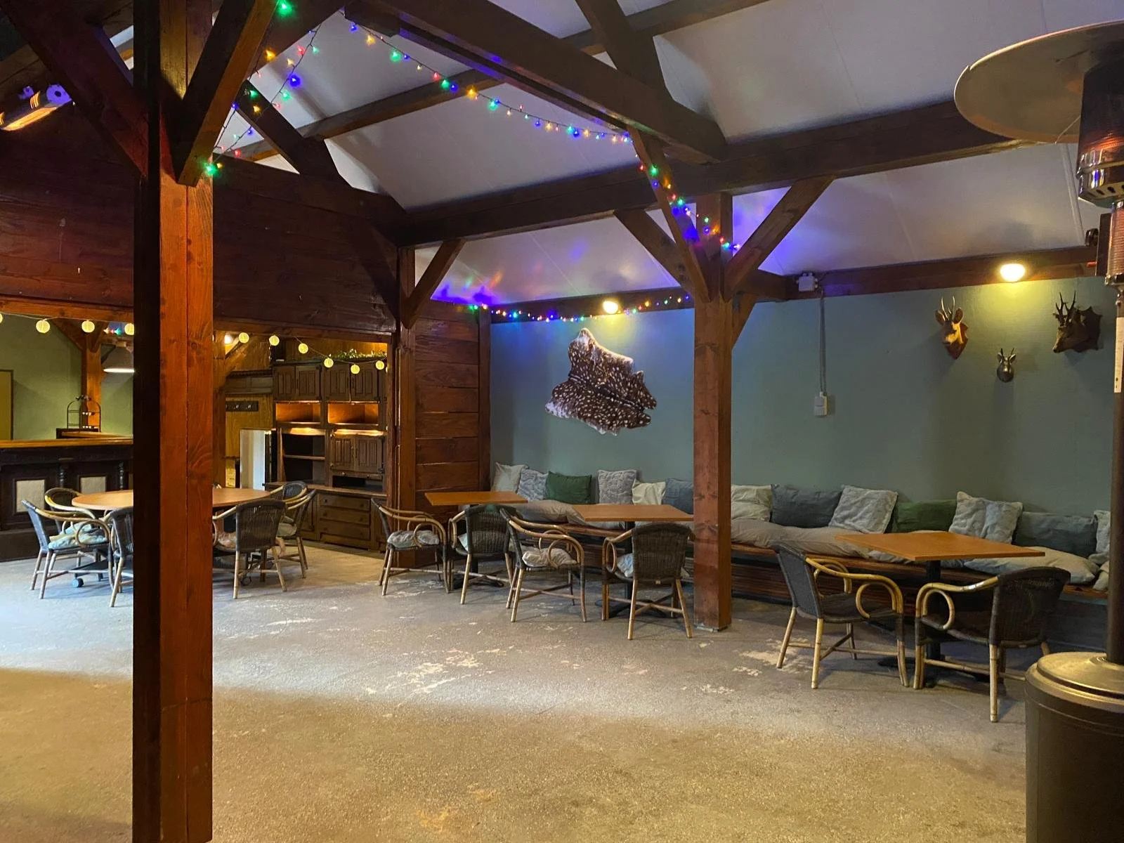 Binnenruimte met houten steunbalken, tafels, stoelen en banken, versieringen zoals gekleurde kerstlampjes en hertenhoofden aan de muur, en decoratief houtkunst op de muur.