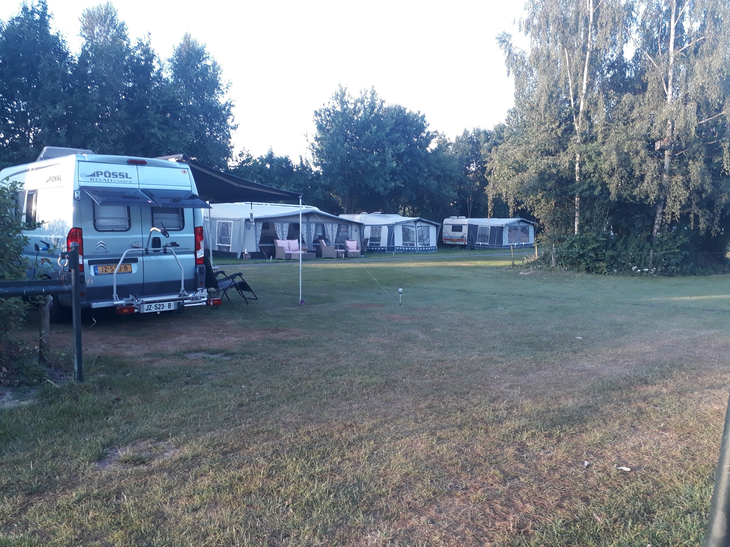 Campinggebied met caravan en tenten in een groene omgeving onder een blauwe hemel.
