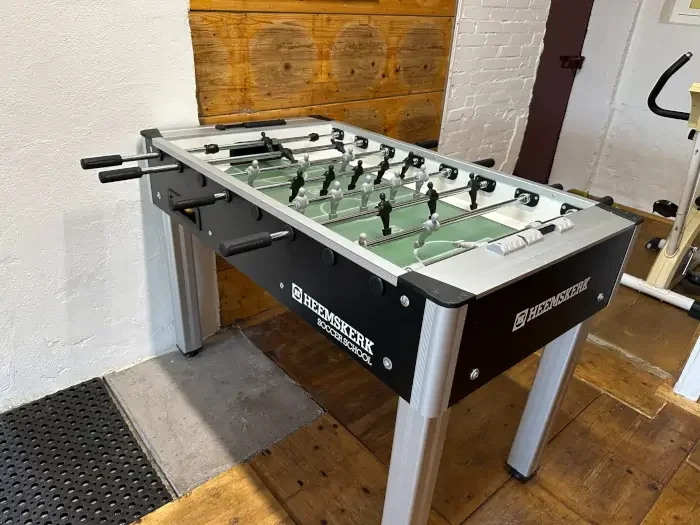 Een tafelvoetbalspel in een kamer met houten vloer en witte muur.