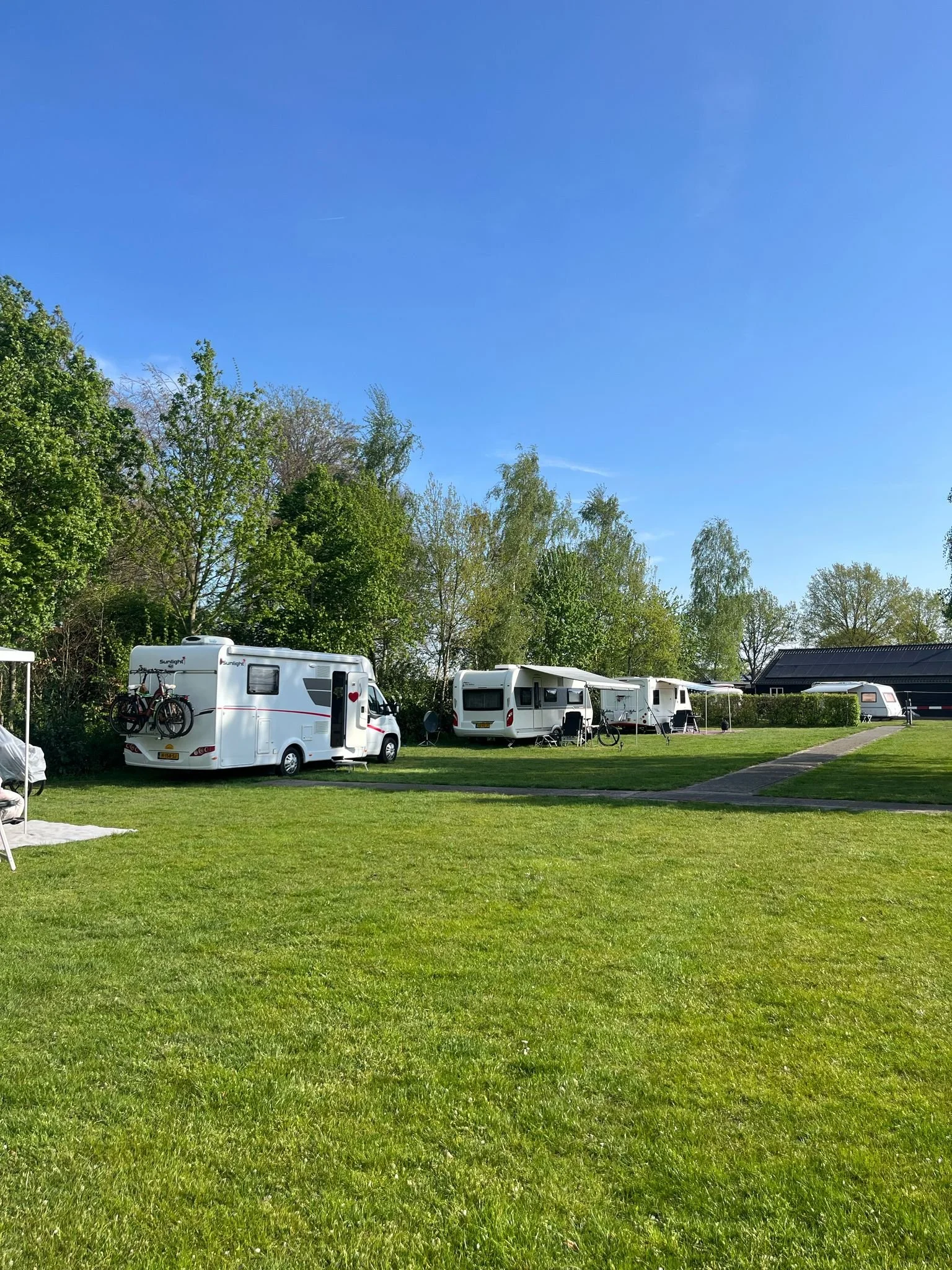 Caravan campside met meerdere caravans op een grasveld onder een blauwe lucht, omringd door bomen.