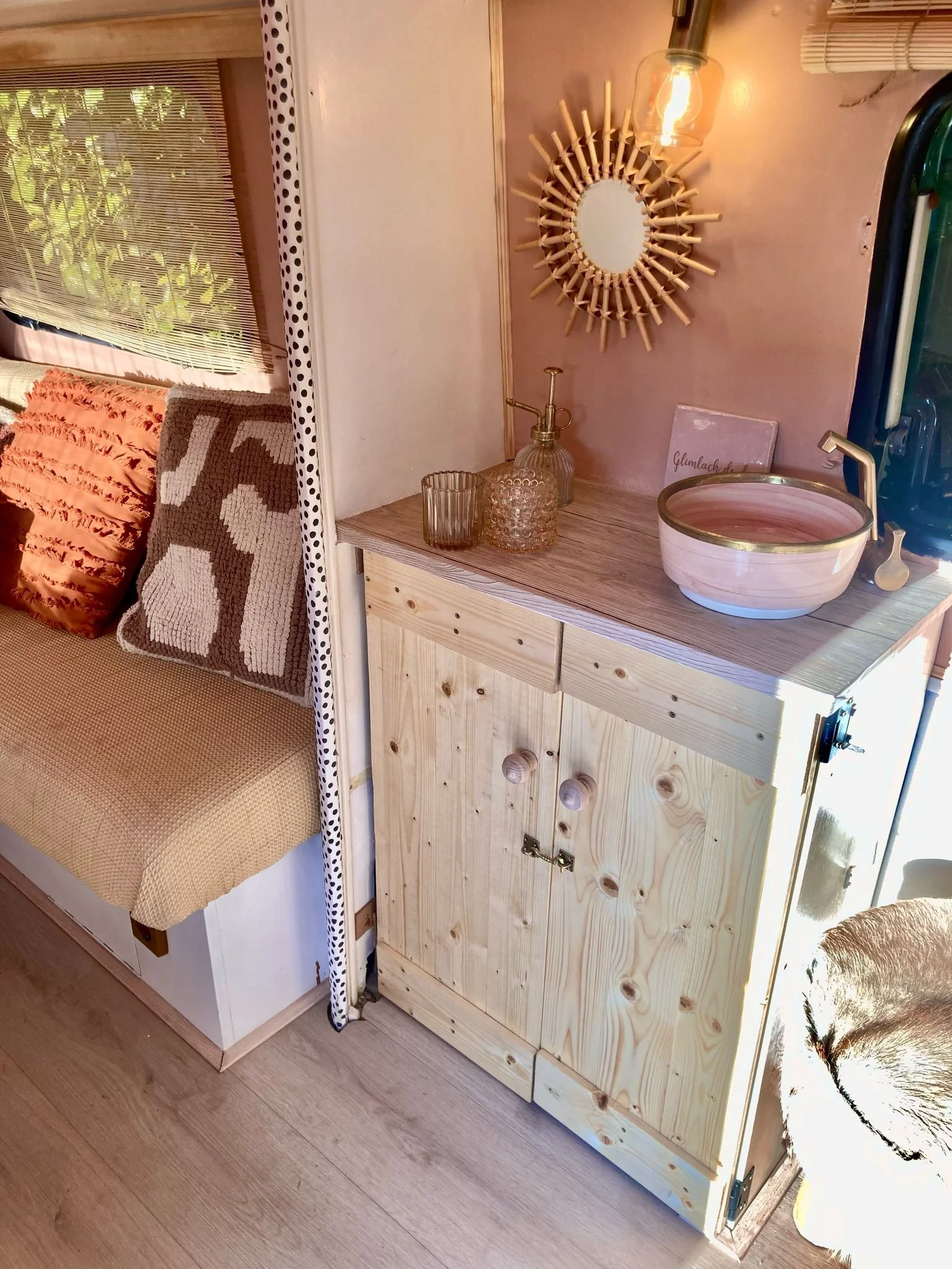 Een houten keukenkast met een wasbak en decoratieve voorwerpen, zoals glazen en een kleine fles, in een gezellig interieur.