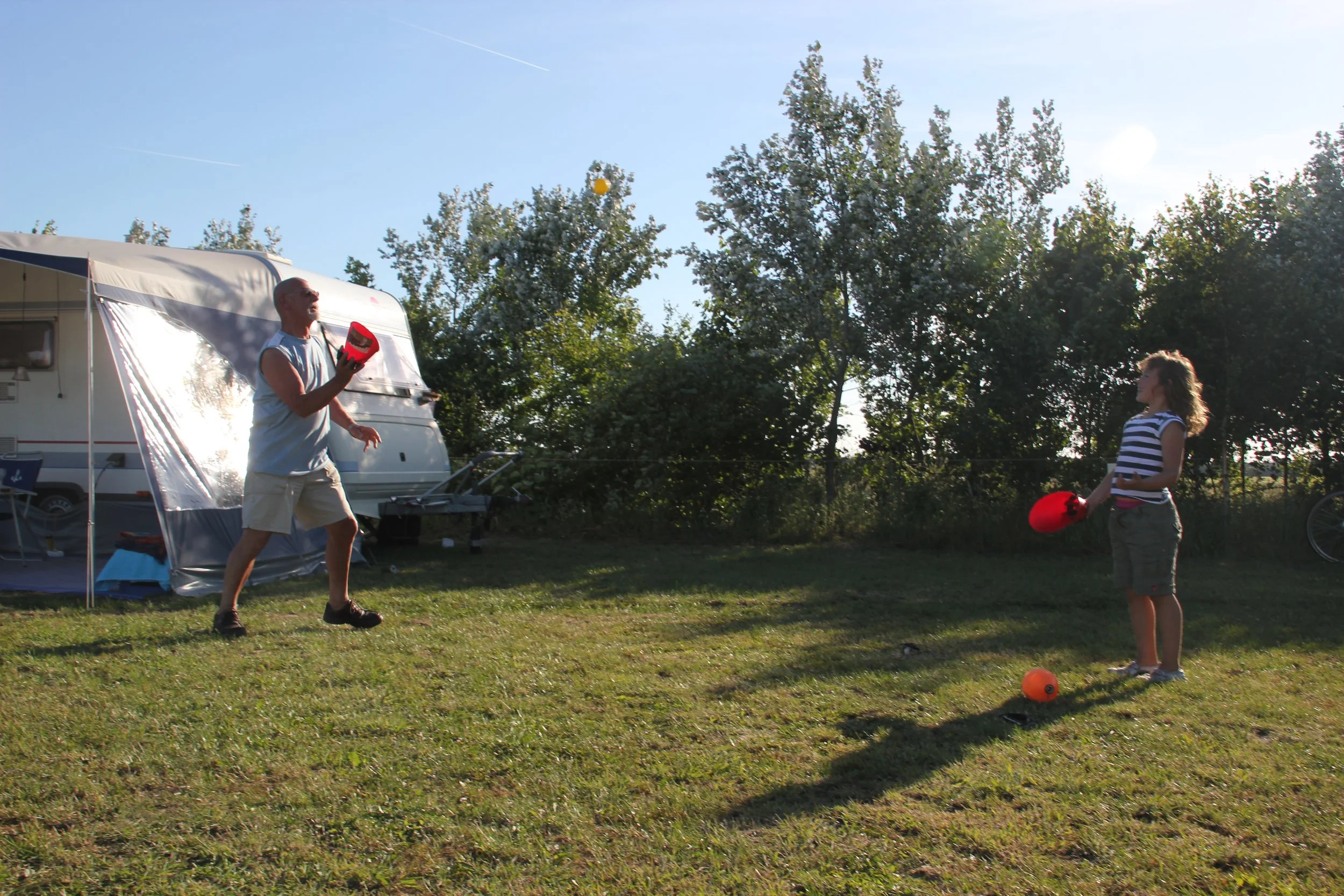 Een man en een meisje die samen spelen met zandlopers of dobbers op een grasveld bij een camper op een zonnige dag.