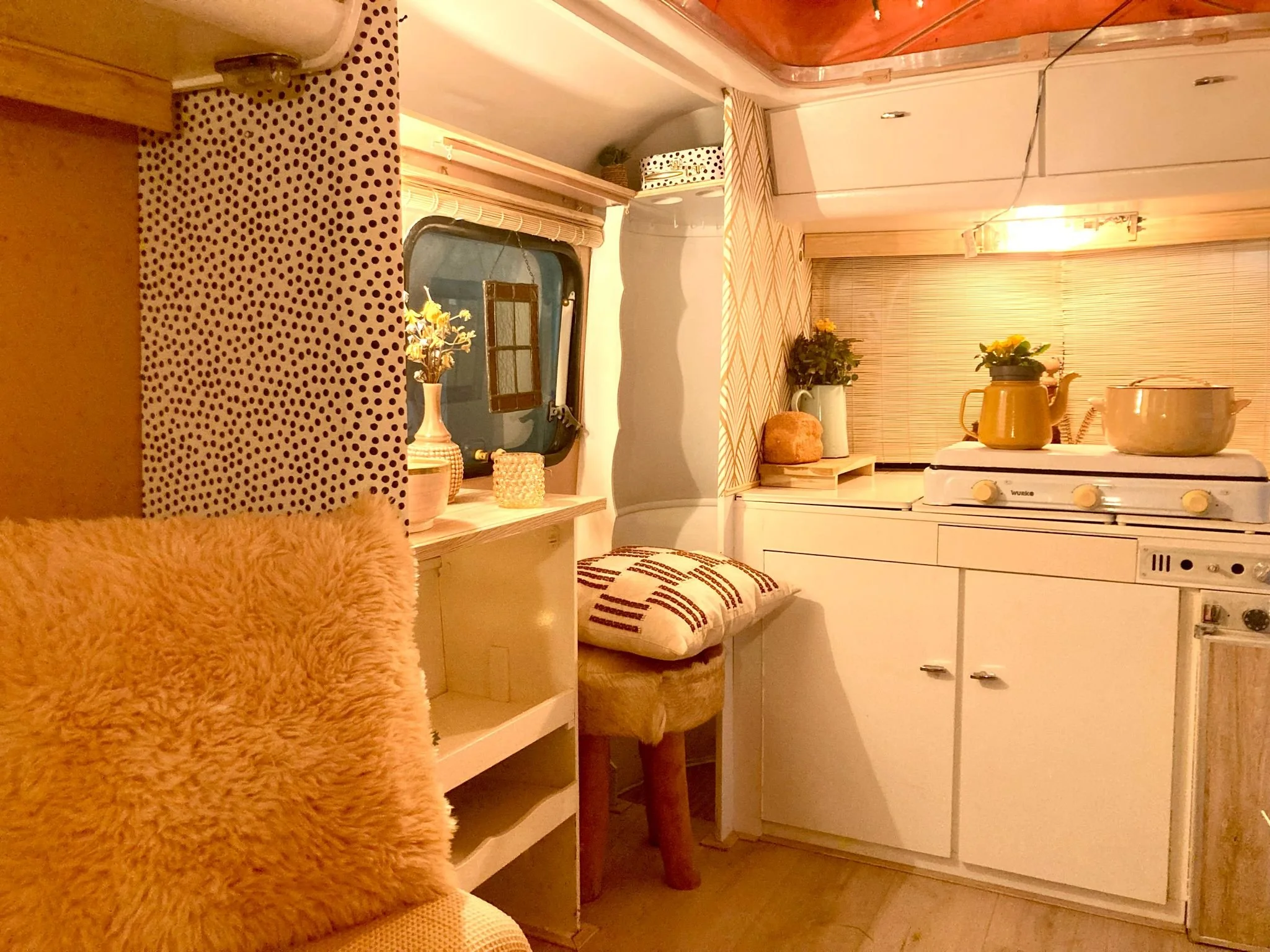 Knusse keuken met witkeuken, thee-ketel, pannen, planten, stoffen accessoires, en decoratie.