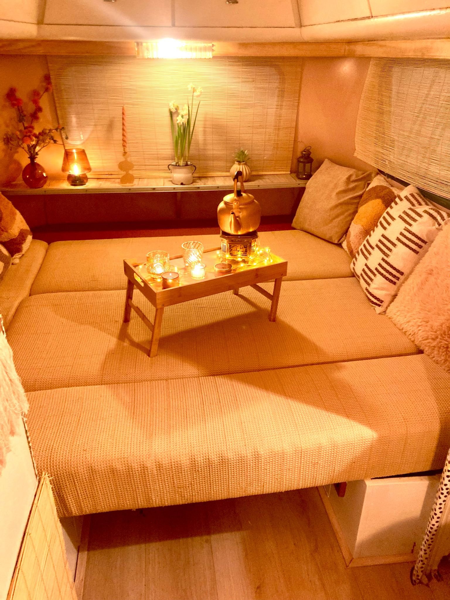 Gedeelde zithoek met kussens en een lage tafel met kaarsen en een ketel, omgeven door gezellige decoraties en planten.