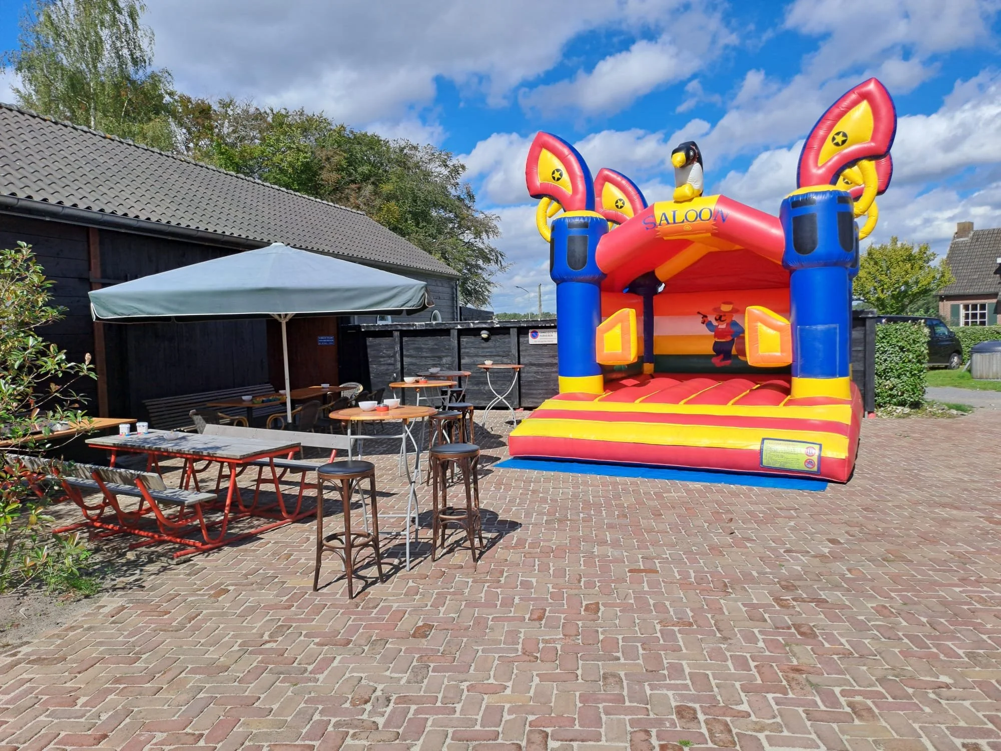 Een kleurrijke stormbaan met een cowboythema op een terras met zitplaatsen en parasol, onder een blauwe hemel.