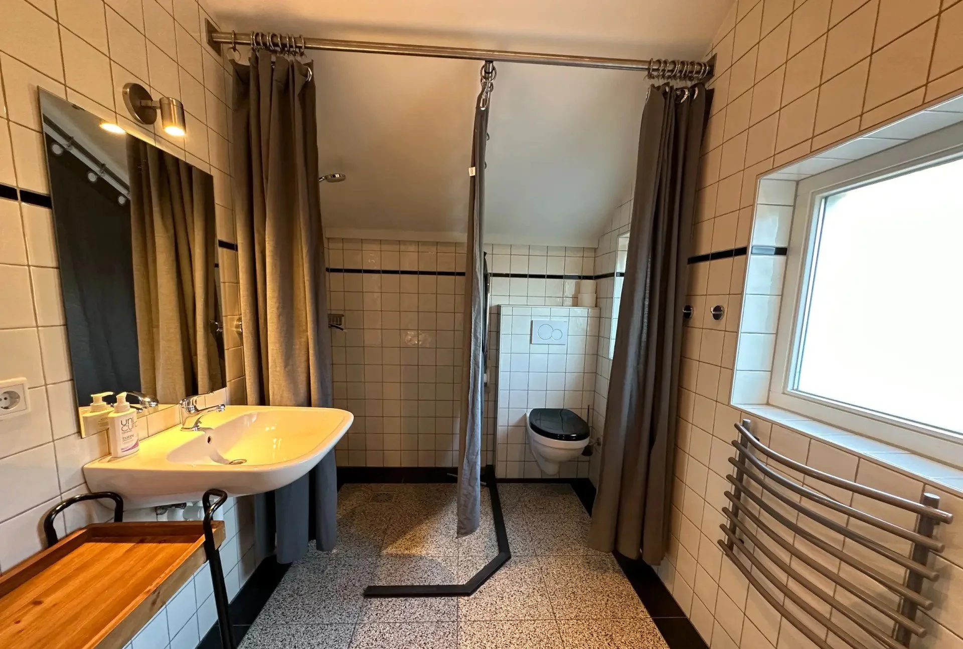 Een openbare badkamer met een wastafel, spiegel, douchecabine, toilet, raam en handdoekradiator.