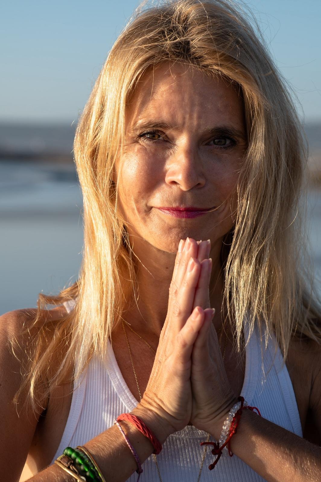 A woman with blonde hair practicing yoga outdoors near a body of water at sunset.