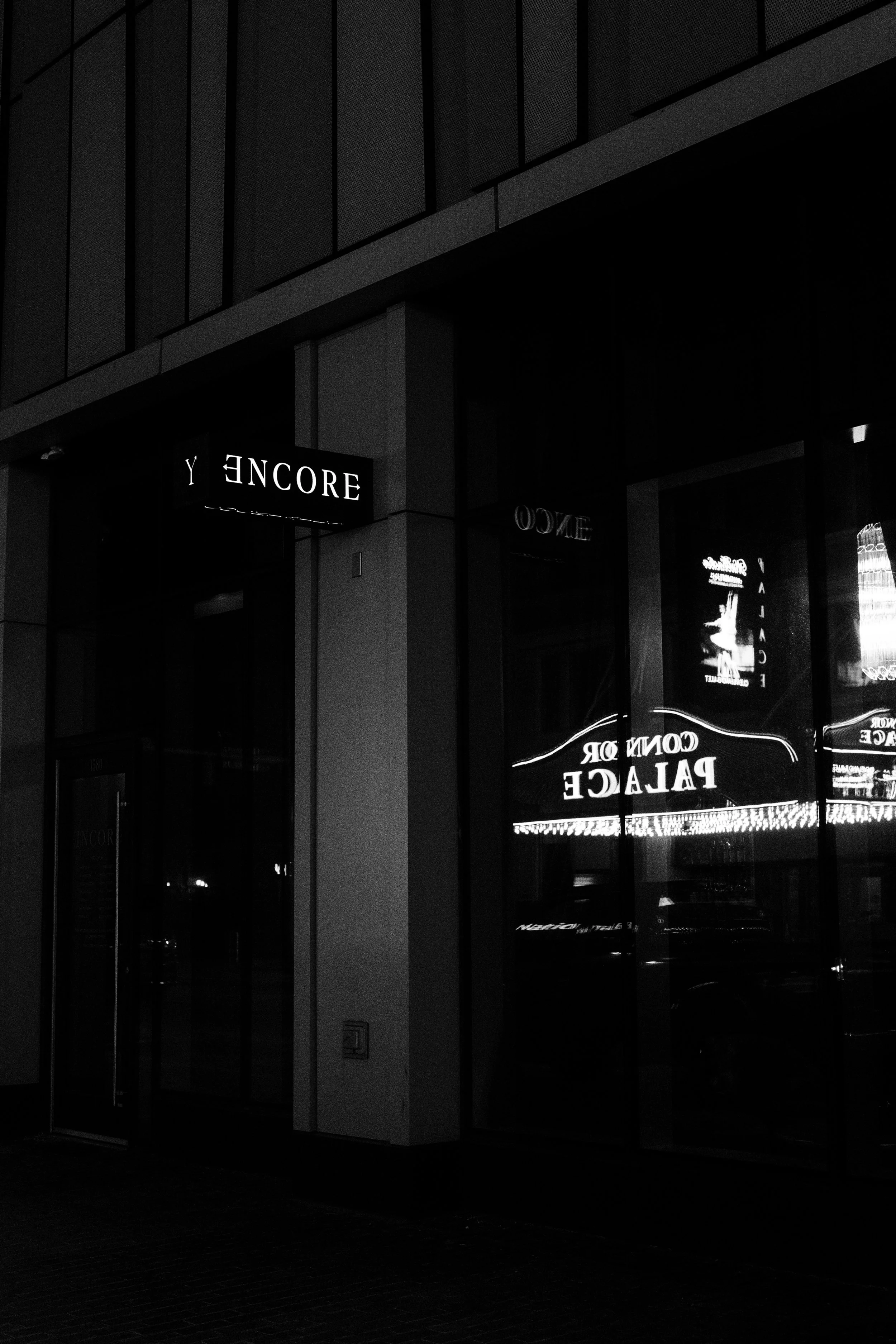 Nighttime city scene with illuminated signs for Encore and Palace, reflected in building windows.