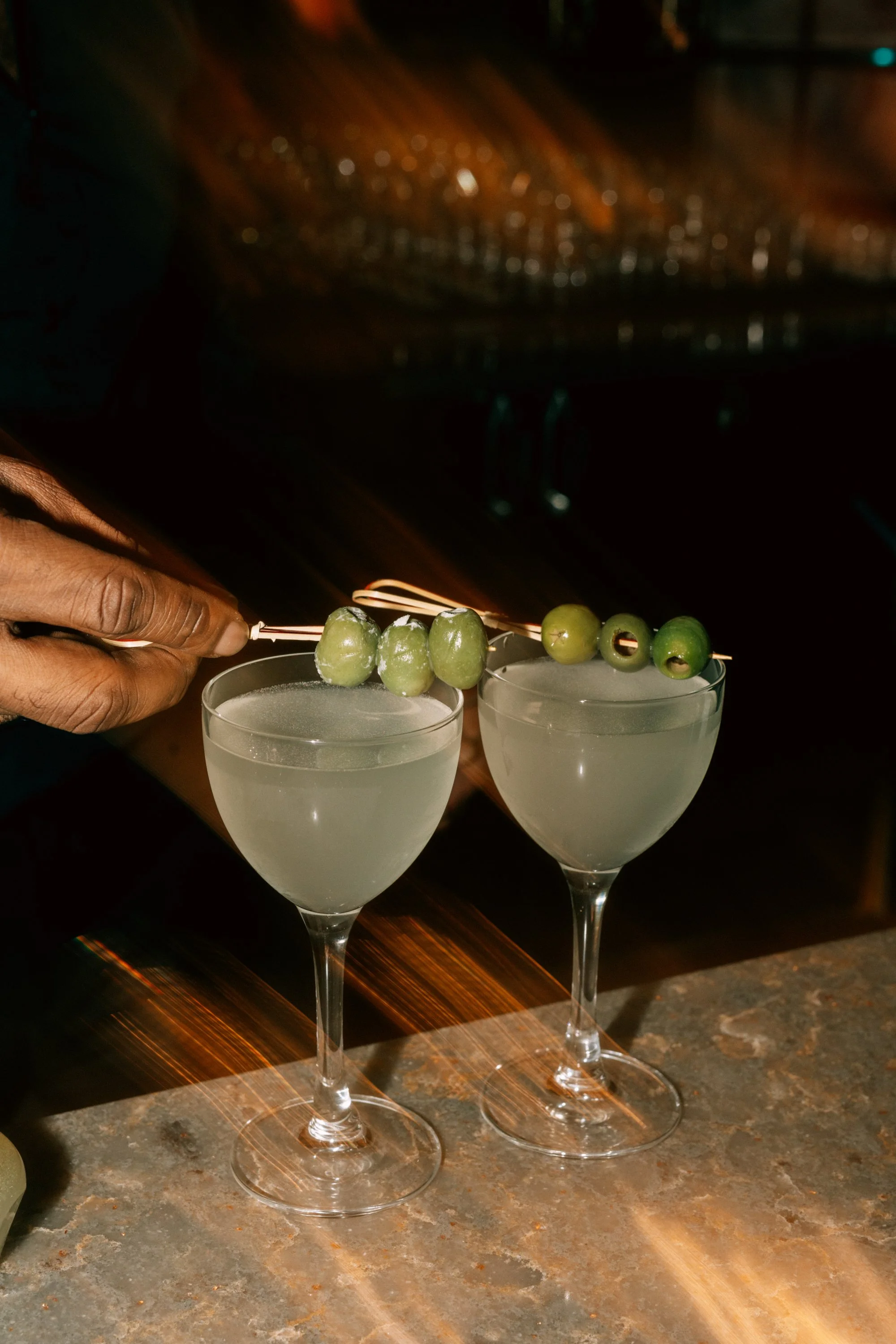 Two cocktails with green olives on skewers garnishing each glass.