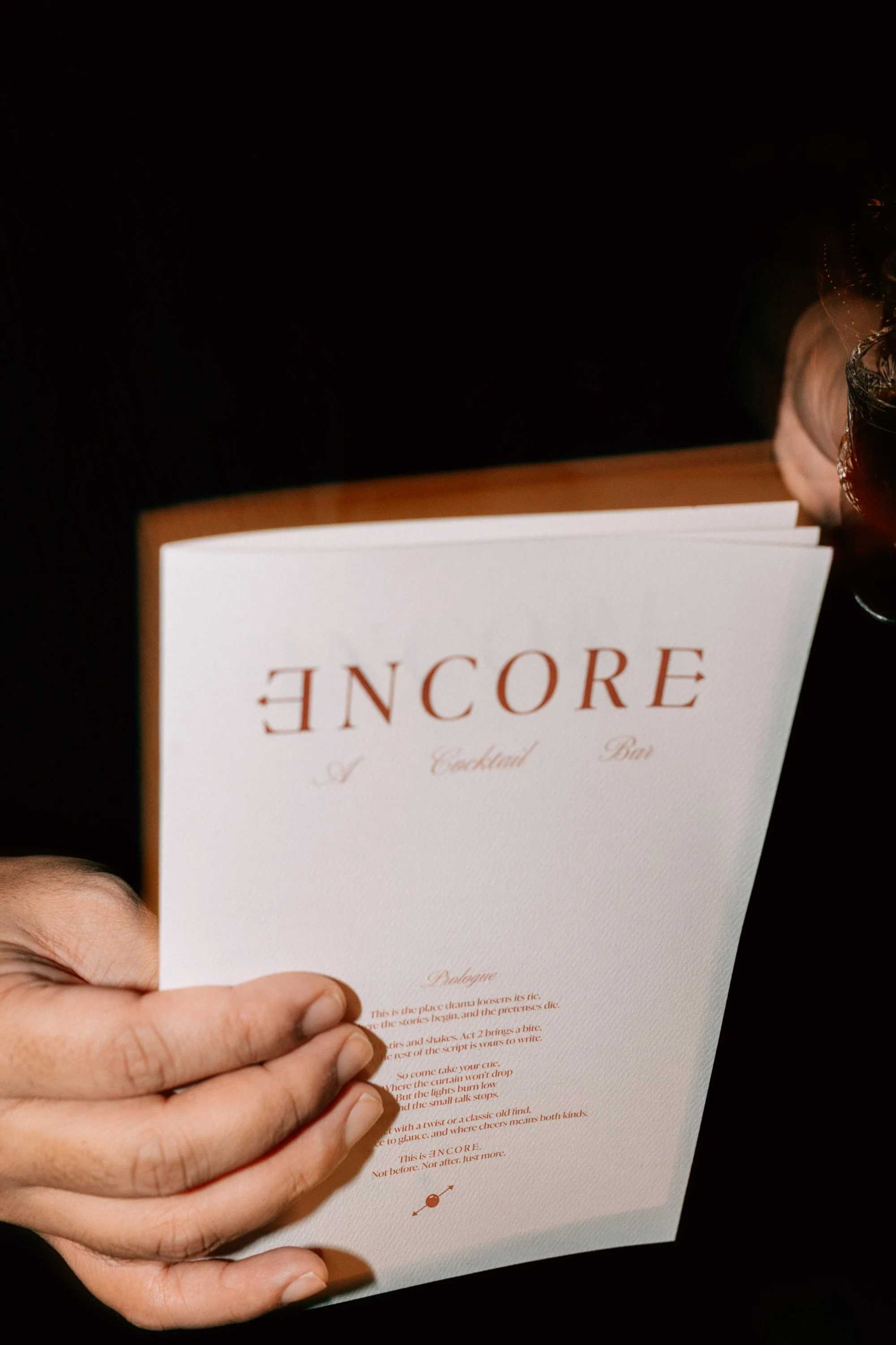 Person holding an event menu titled 'ENCORE' with a cocktail bar description.