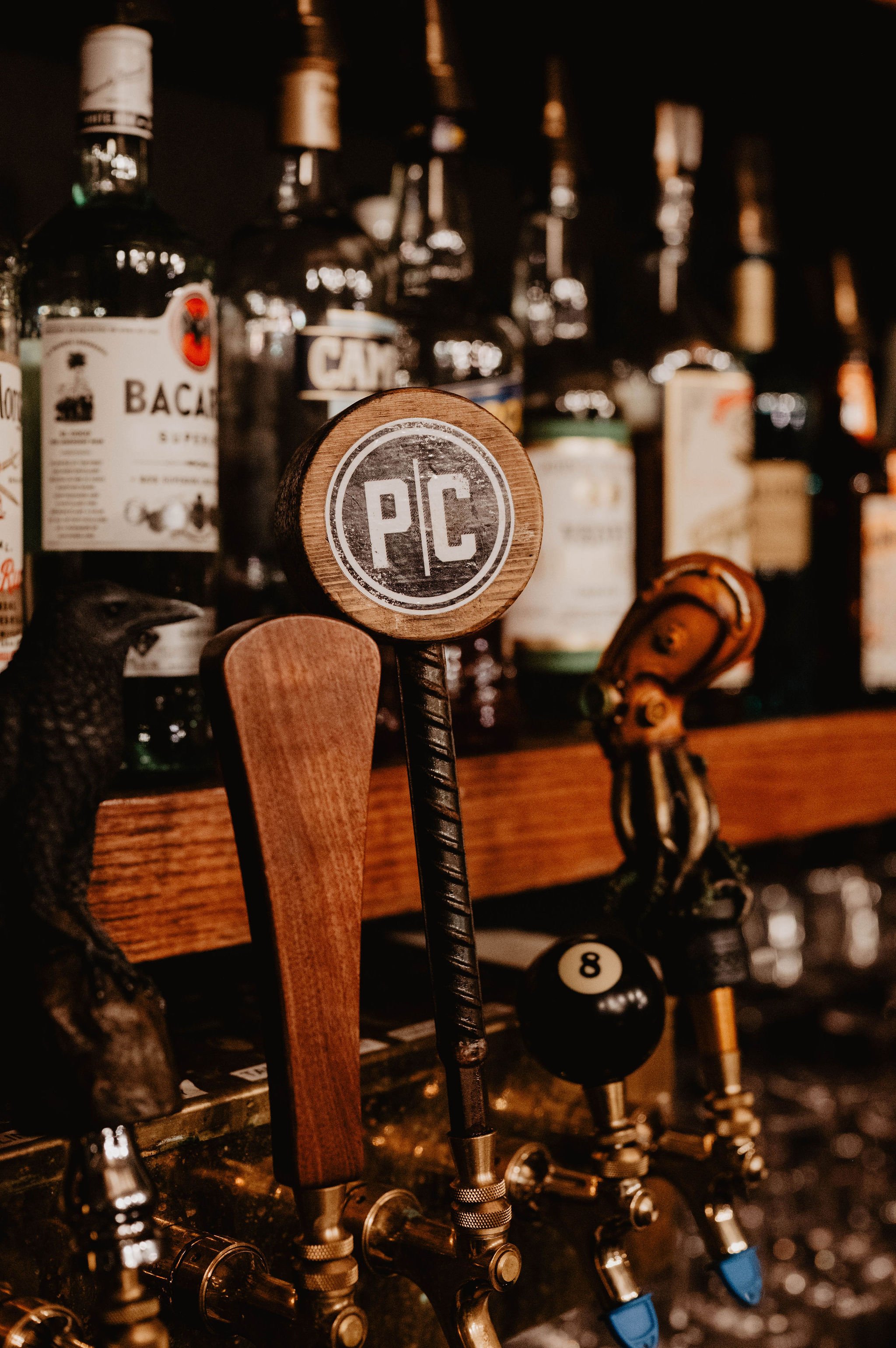 Close-up of bar taps with wooden handles, logos, and bottles of alcohol in the background.