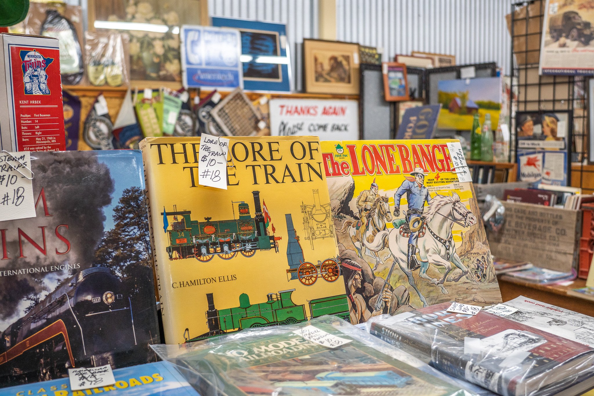 Books about trains, horses, and history displayed on a table at a store or auction, with various framed pictures and signs in the background.