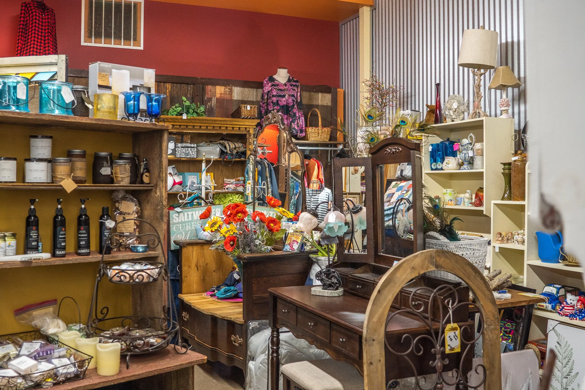 Interior of a thrift store with various furniture, clothing, and decorative items displayed on shelves and tables.