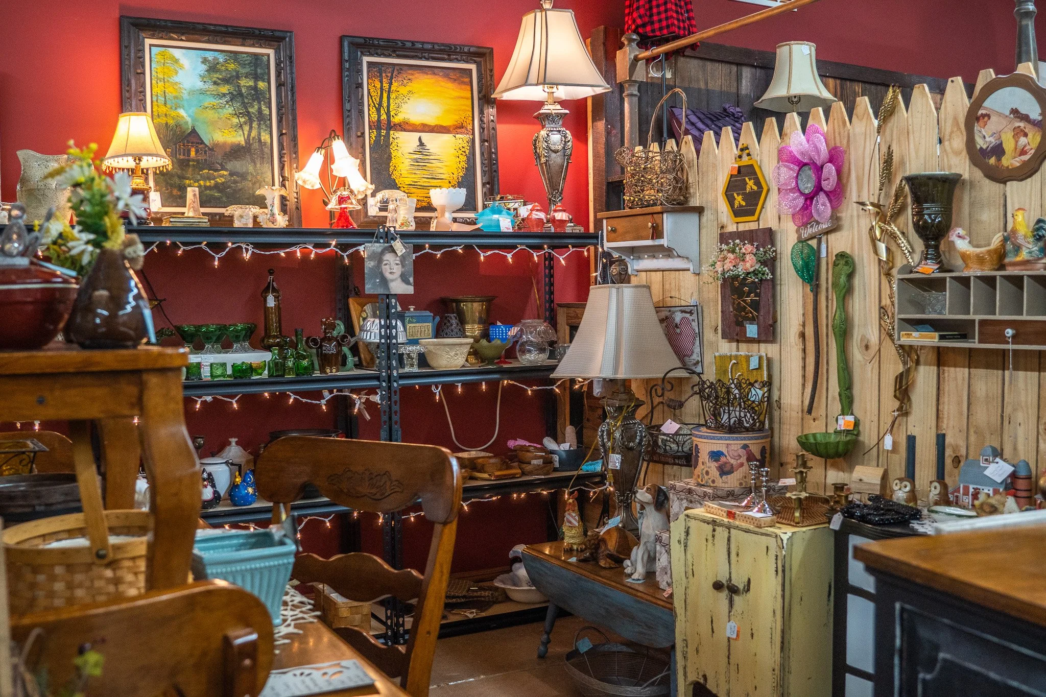 Interior view of an antique store with shelves and tables displaying various decorative items, lamps, paintings, and knickknacks.