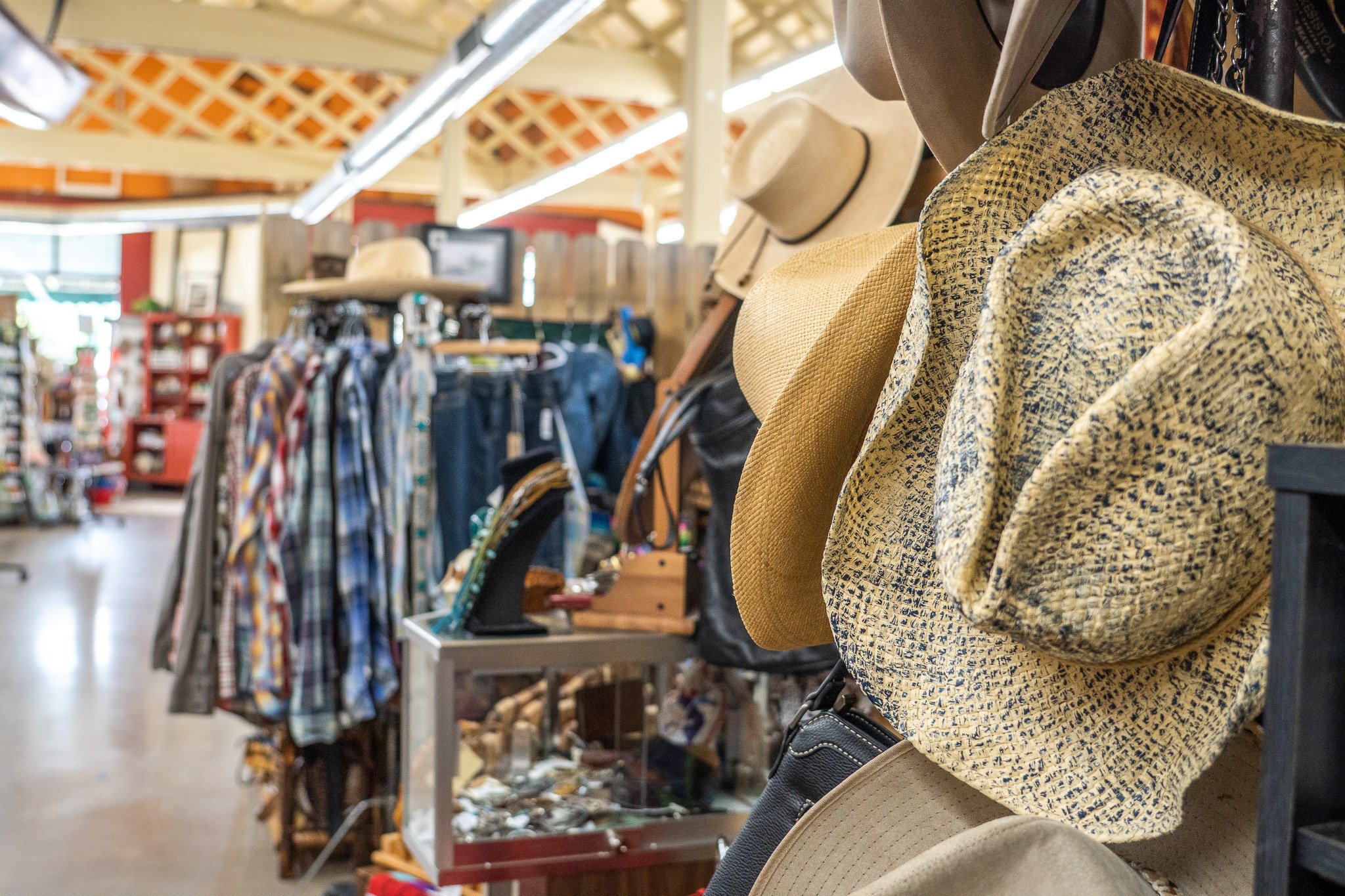 Close-up of straw hats hanging on display at a thrift store, with clothing racks and other items in the background.