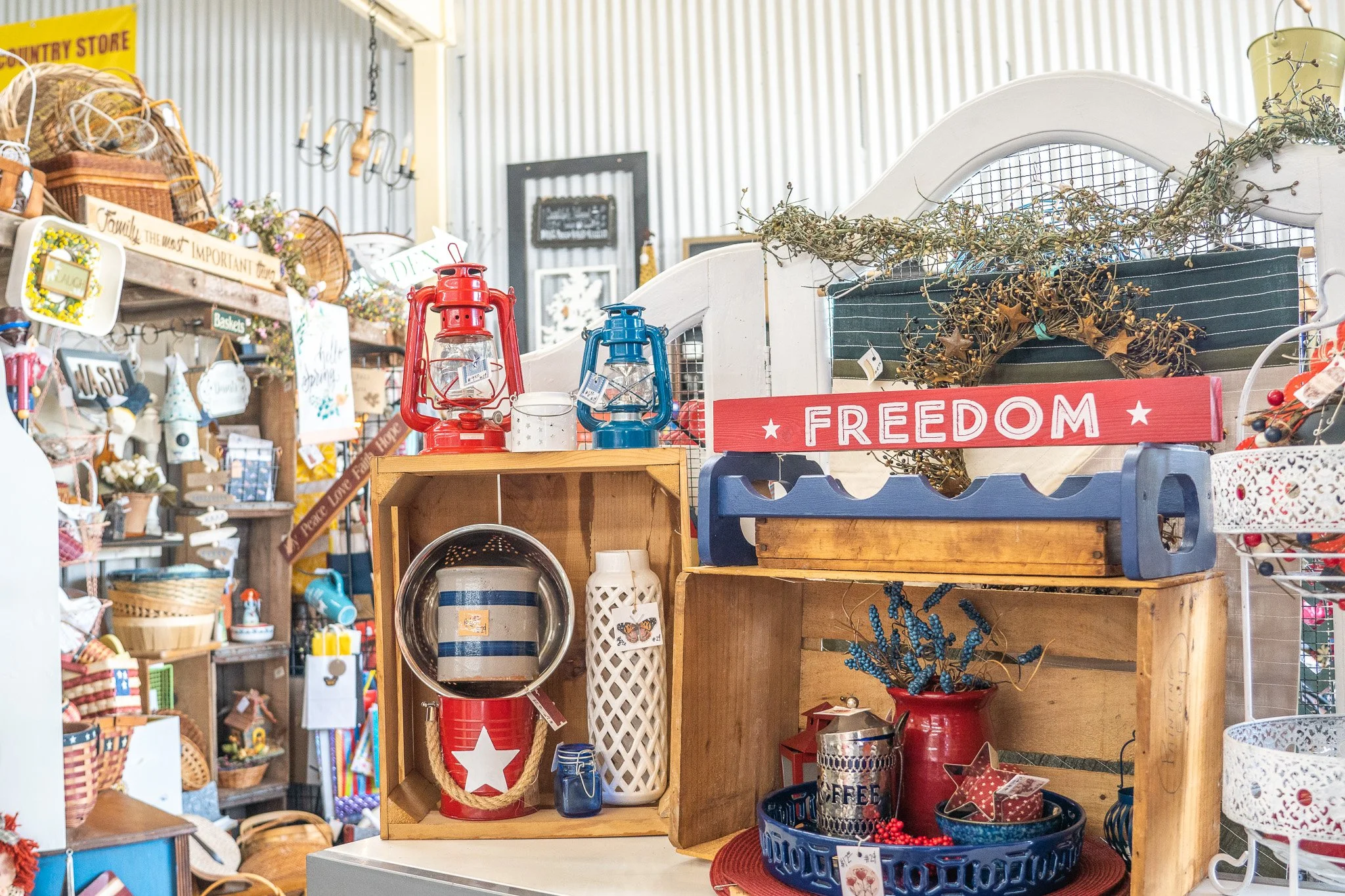 Display of decorative items with a red sign reading "FREEDOM," lanterns, a woven star, and patriotic-themed decor at a store.