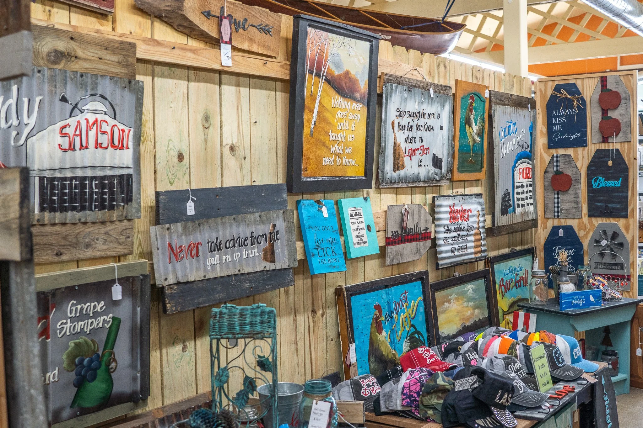 Wall displays various rustic signs with quotes and messages, along with baseball caps and small accessories for sale.