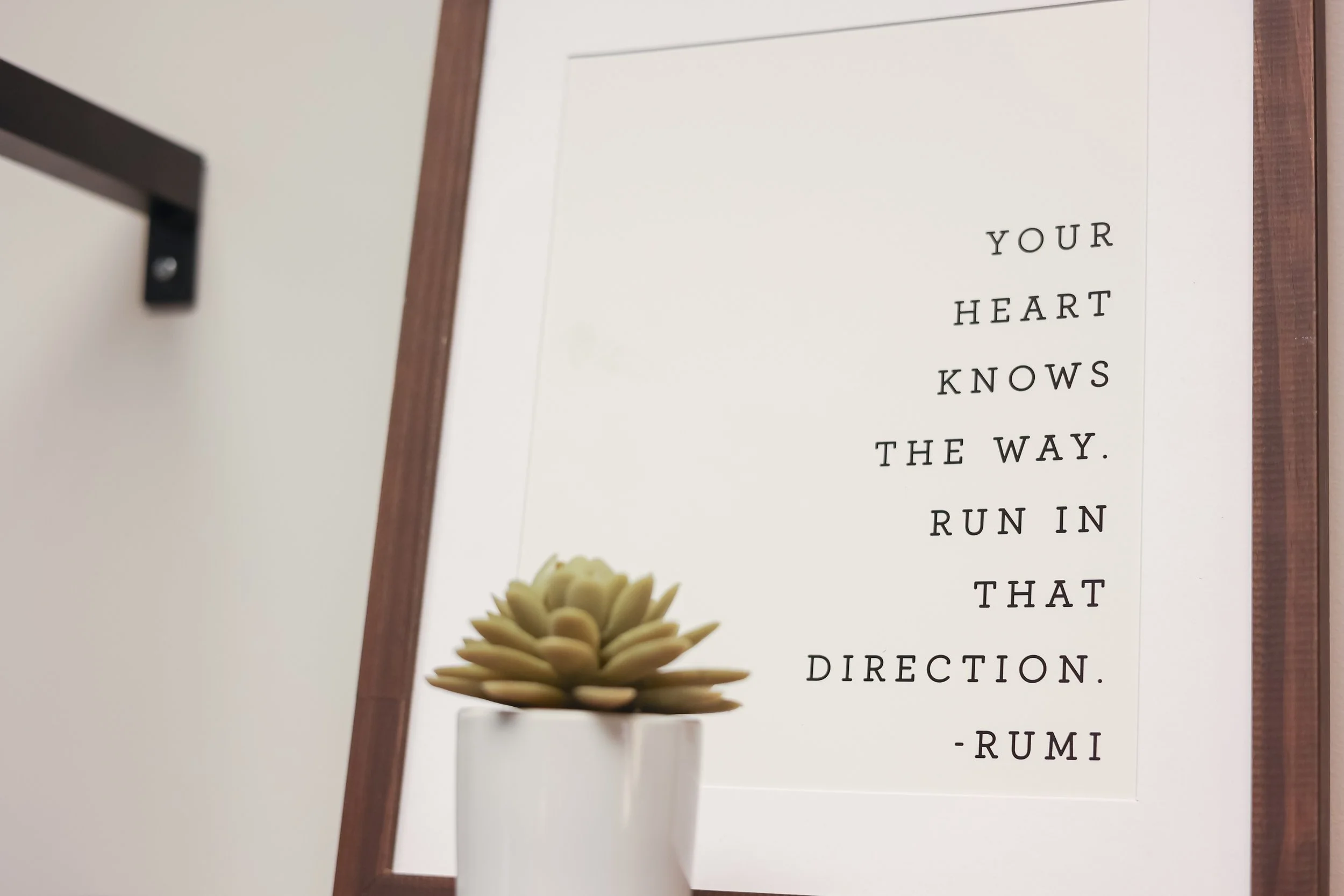 A framed quote on the wall reads, "Your heart knows the way. Run in that direction. - Rumi" with a small potted succulent plant in front of it. Decor in the lobby at GR Therapy Collective